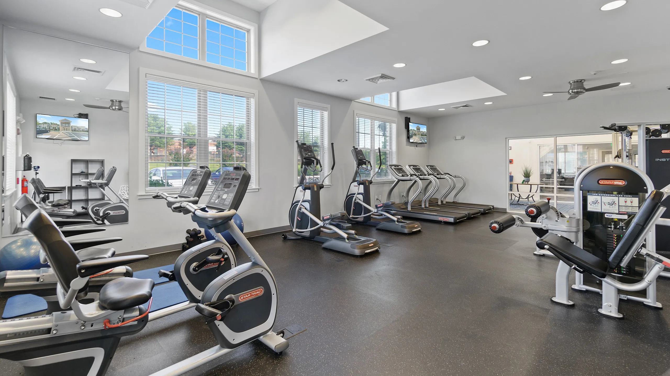 Bright and modern fitness center featuring state-of-the-art cardio equipment and weight machines, with ample natural light and spacious workout areas.