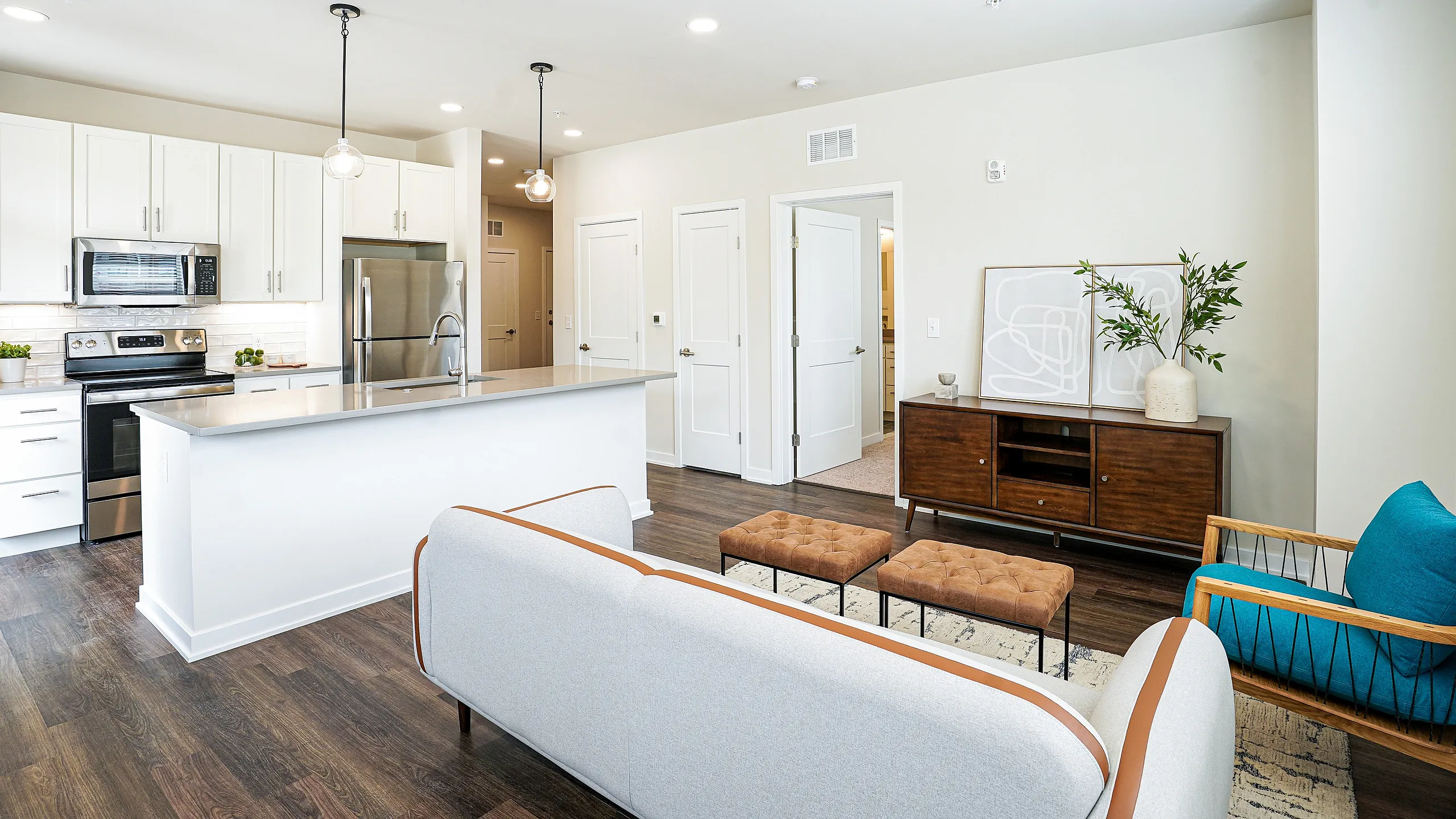 Modern open-plan kitchen and living room featuring sleek white cabinetry, stainless steel appliances, a cozy seating area, and stylish wooden flooring.