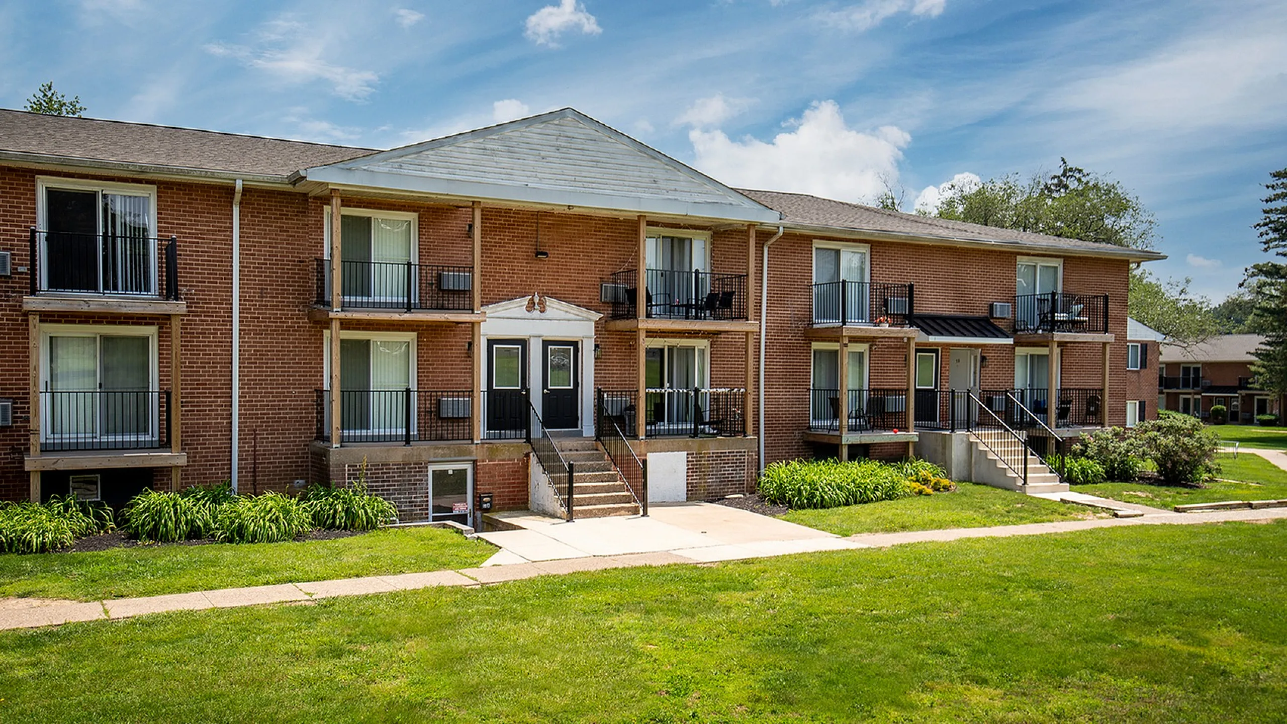 Inviting two-story brick apartment building with charming balconies, surrounded by lush greenery and a well-maintained lawn.
