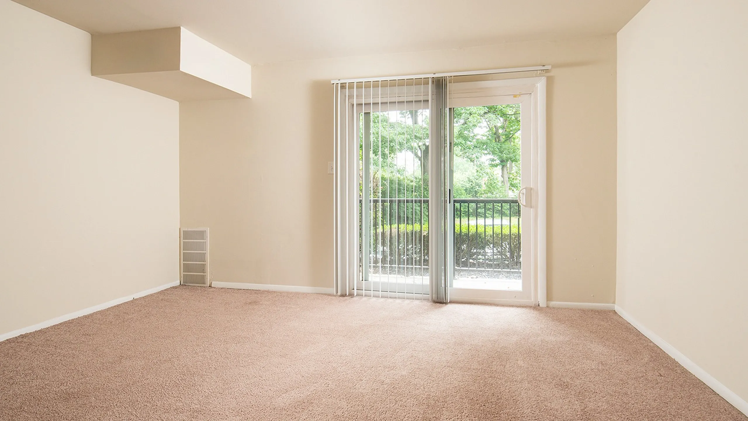 Bright living room with plush carpeting and sliding glass doors opening to a scenic balcony view.