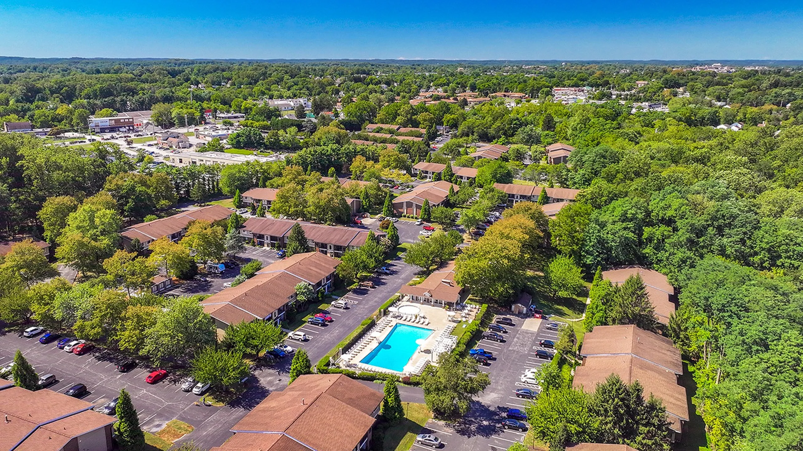 Scenic aerial view of lush green residential community with central swimming pool surrounded by charming houses and vibrant foliage.