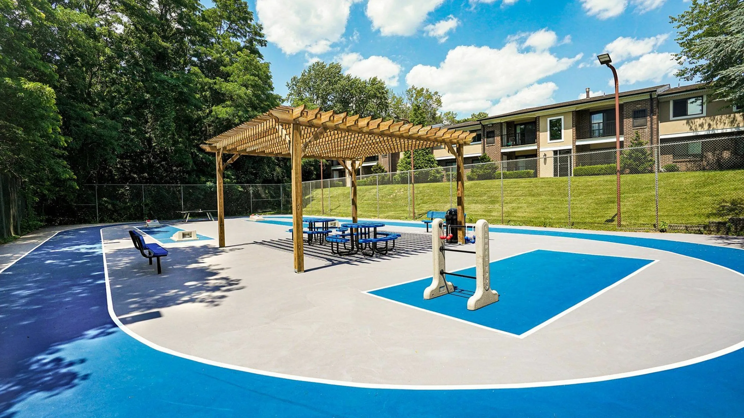 Inviting community recreation area with spacious outdoor seating, basketball court, and charming pergola providing shade under a bright blue sky.