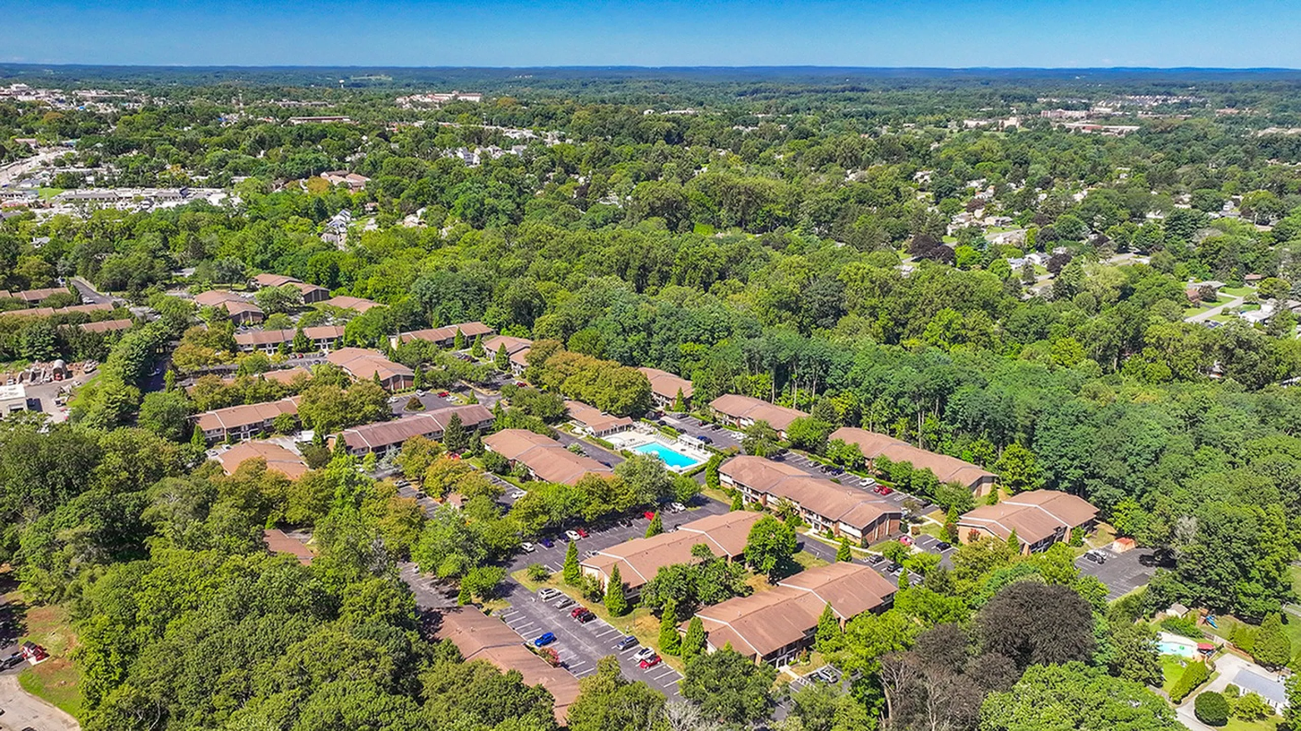 Aerial view of a serene residential complex nestled in lush greenery with modern amenities and a central pool, offering a tranquil suburban lifestyle.