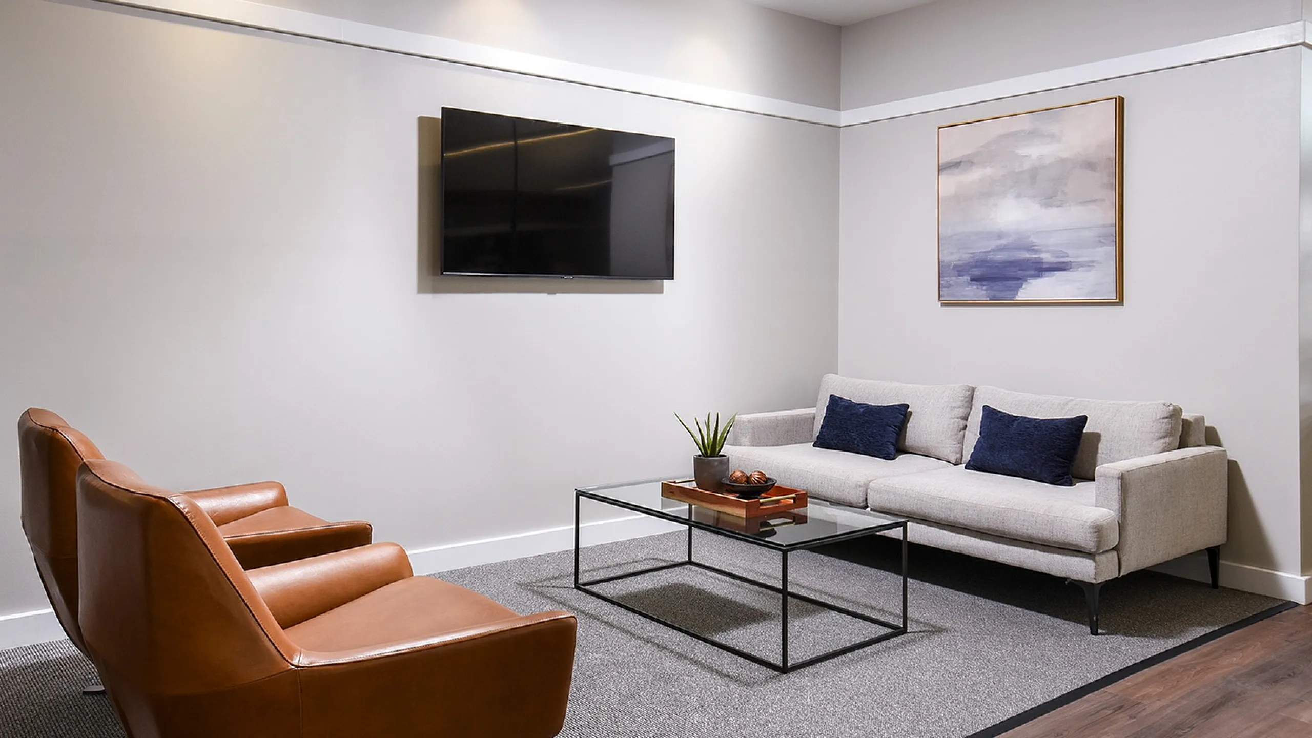 Elegant living room with modern decor, featuring a sleek white couch, brown leather armchairs, wall-mounted TV, and abstract art piece.