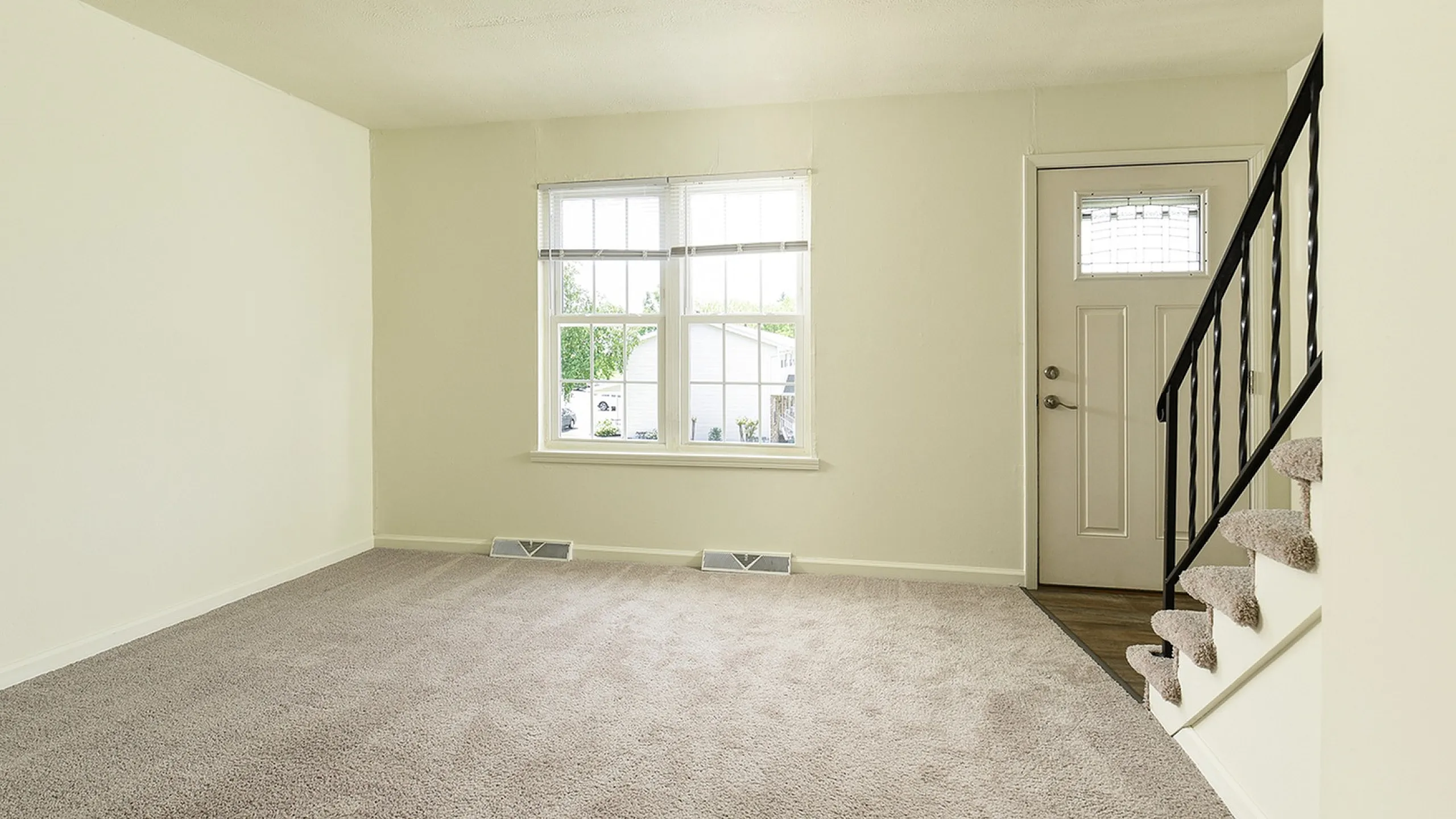 Bright living room with plush carpeting, elegant staircase, and large window inviting natural light.