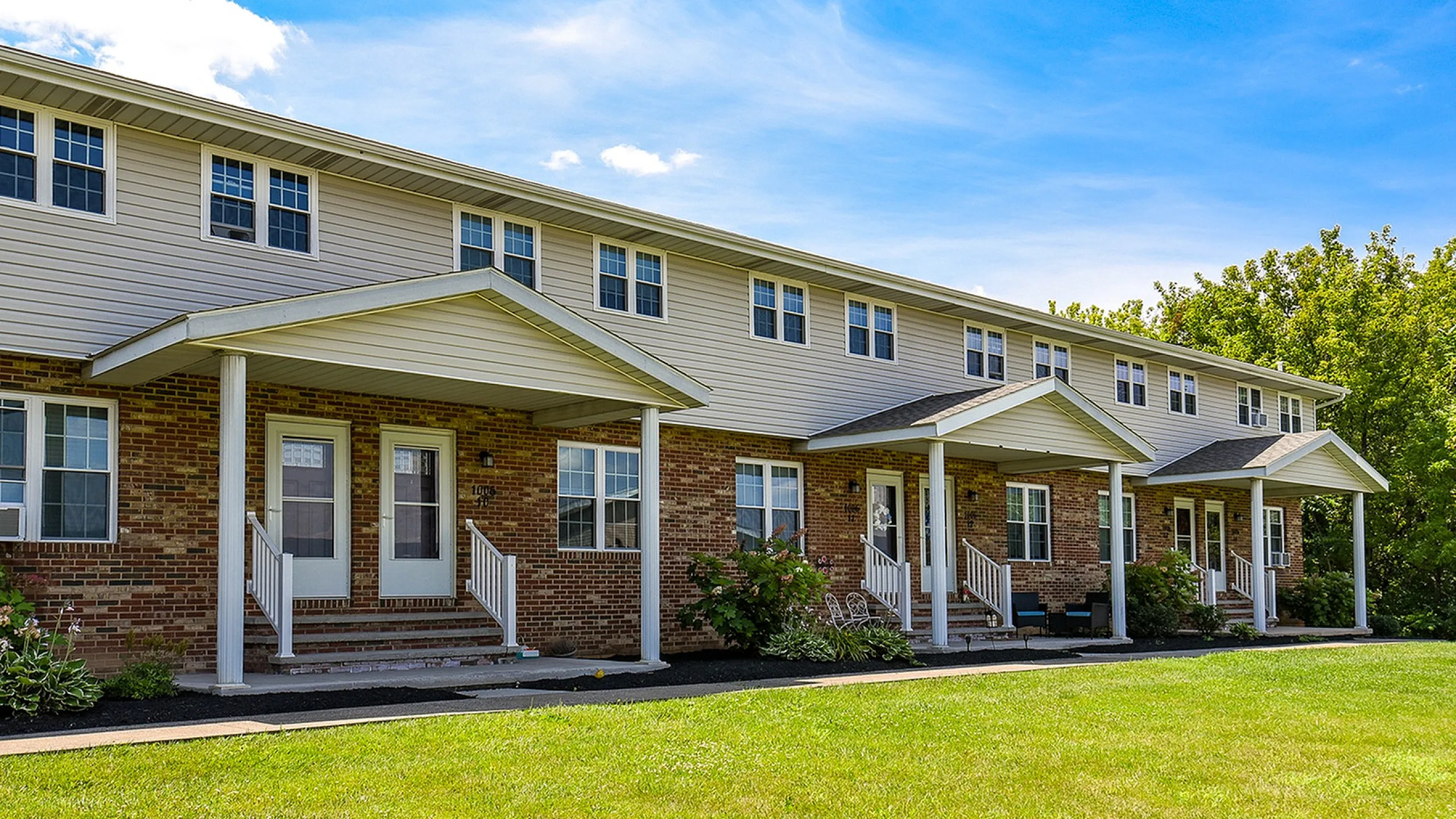 Charming row of townhouses with welcoming front porches, set against a bright, clear sky and lush greenery.