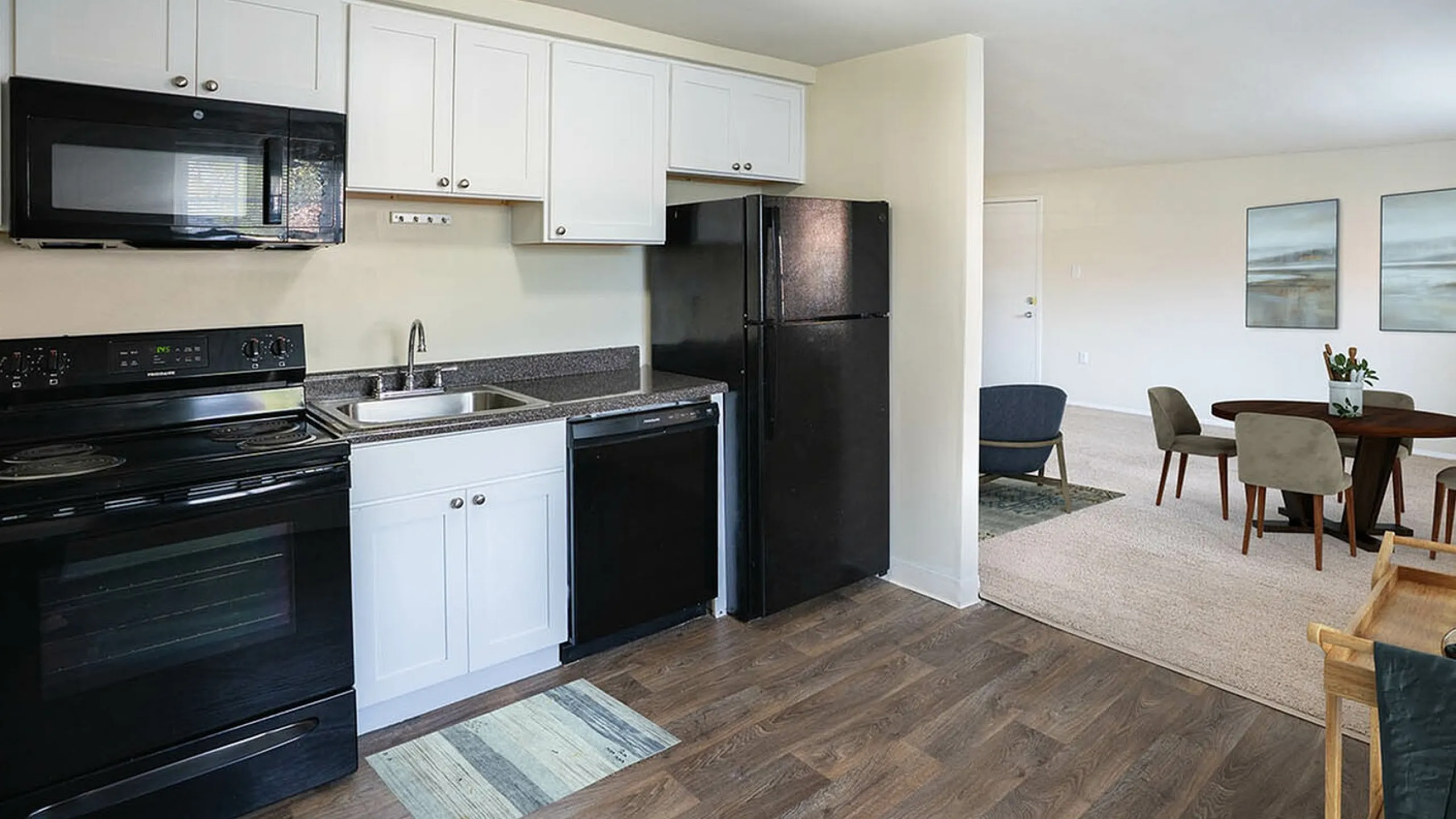Modern kitchen with sleek black appliances and spacious white cabinets opening into a cozy dining area with elegant table and chairs.