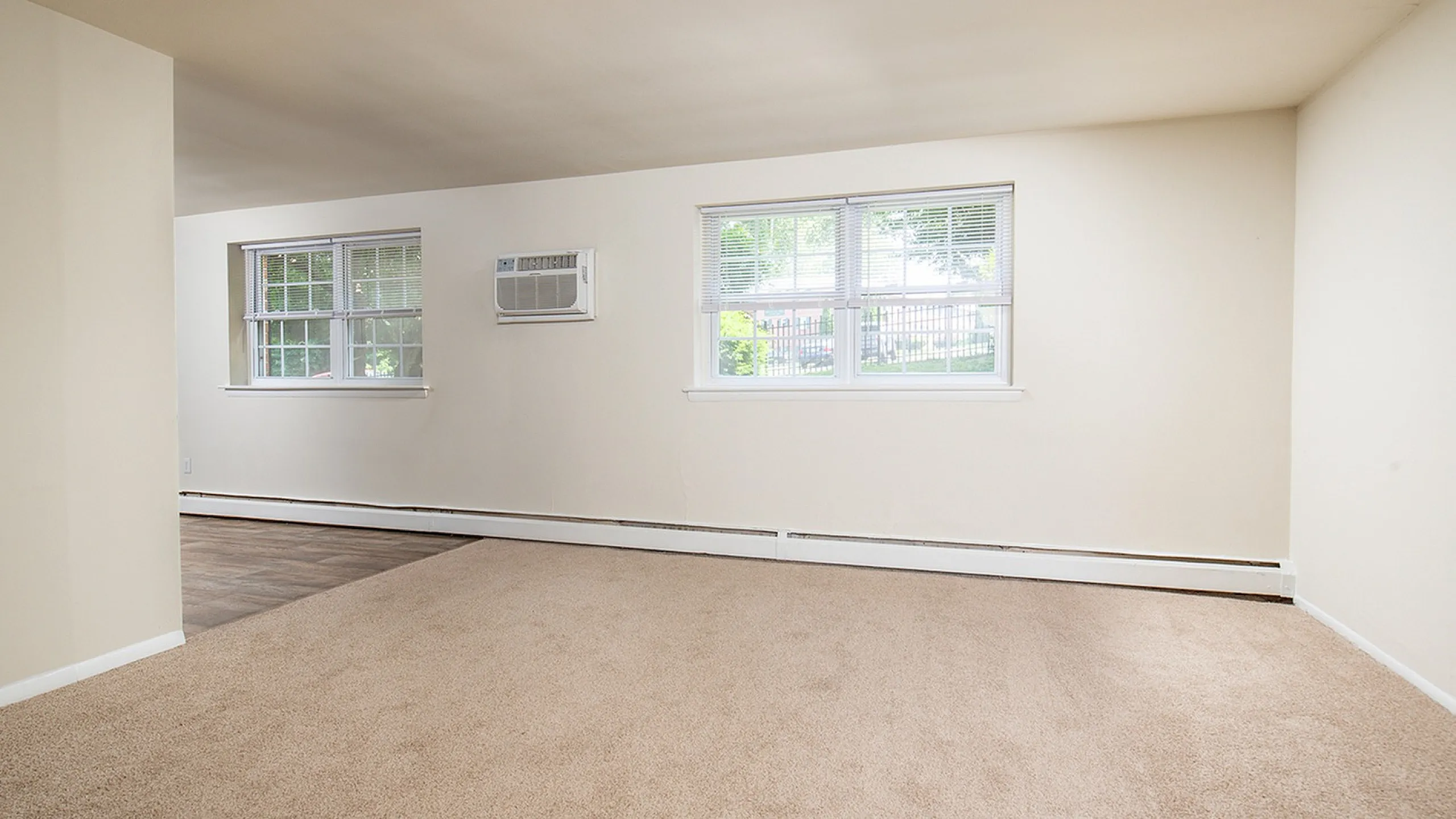 Bright, spacious interior with large windows, neutral carpeting, and wooden flooring, perfect for a cozy living area.