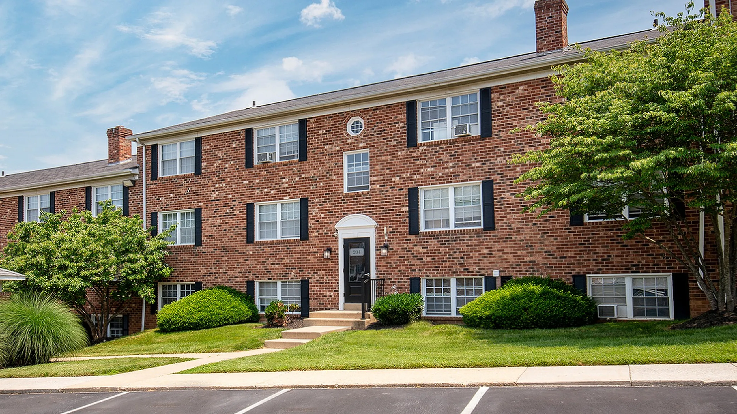 Charming brick apartment building with classic architecture, surrounded by lush greenery and a well-maintained lawn.