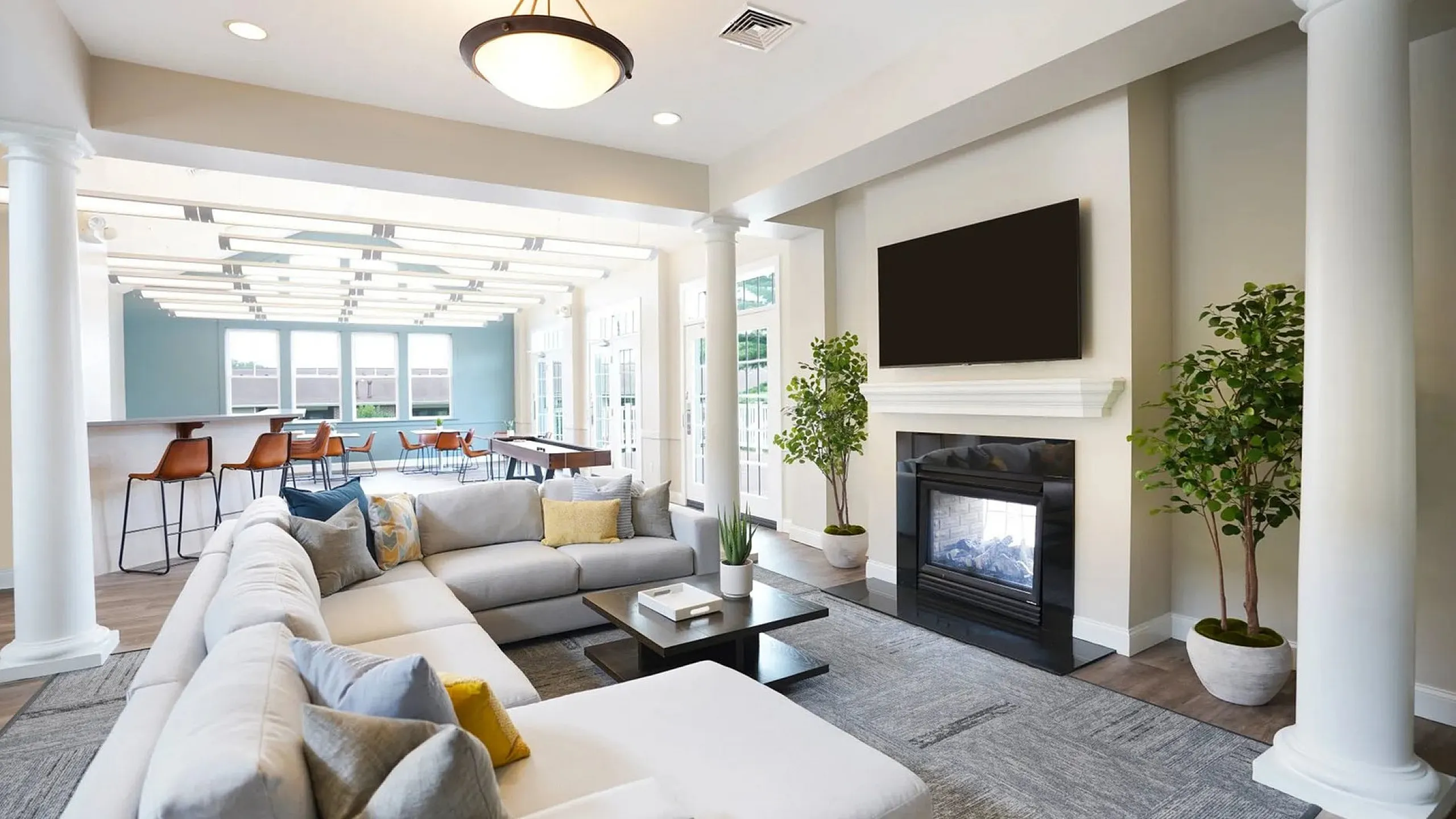 Luxurious living room with modern sectional sofa, elegant fireplace, and open-plan design leading to a stylish dining area with high stools.
