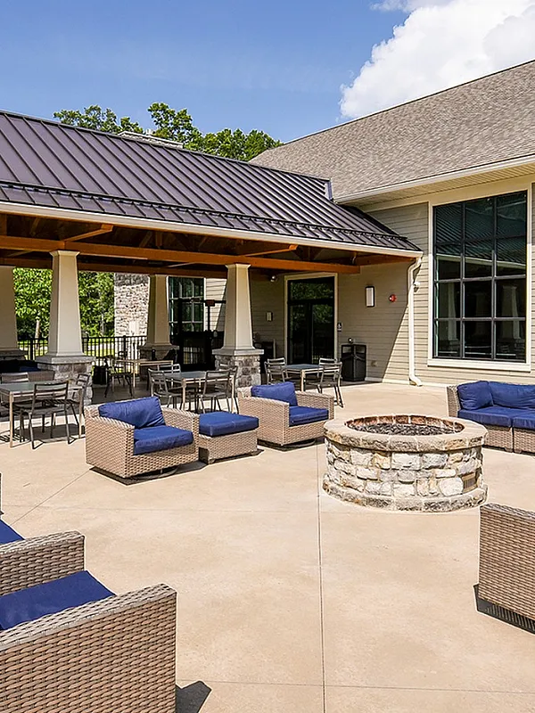 Luxurious outdoor patio with woven furniture, cozy fireplace, and elegant stone columns under a sunlit sky.