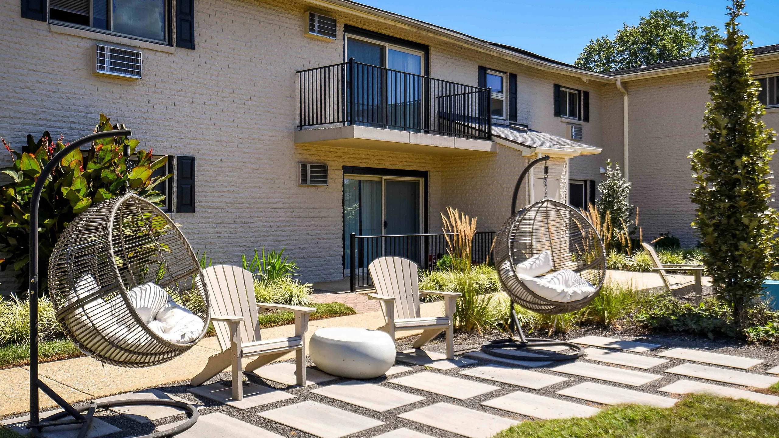 Charming courtyard with stylish outdoor seating, including hanging lounge chairs and Adirondack chairs, surrounded by vibrant greenery and contemporary architecture.