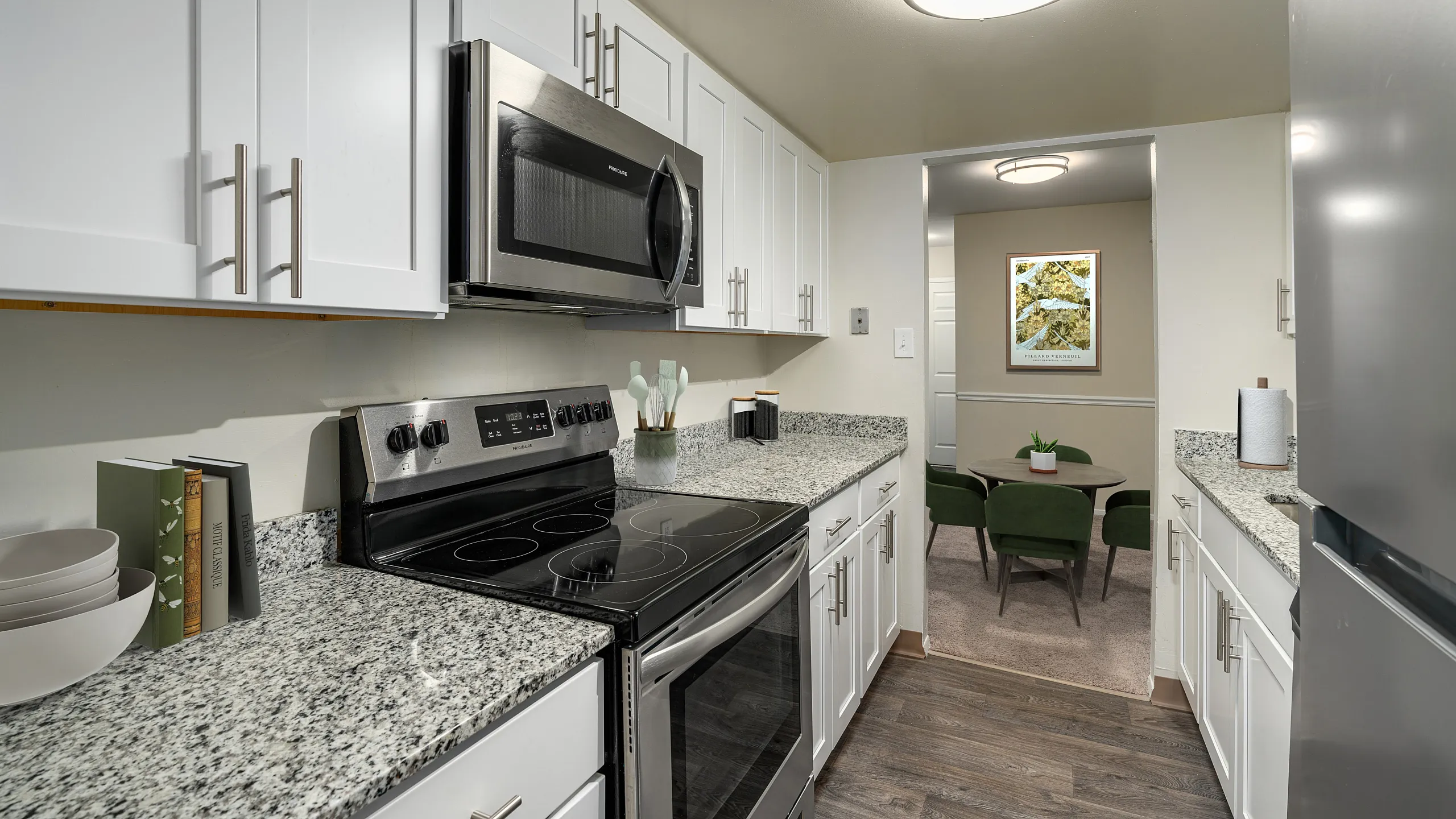 Modern kitchen with sleek stainless steel appliances, granite countertops, and elegant white cabinetry; opens into a cozy dining area with stylish green chairs.
