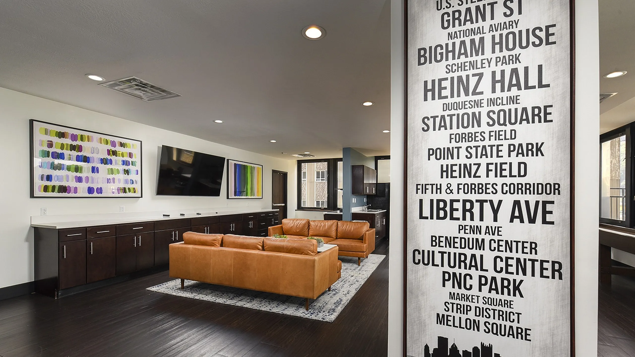 Modern apartment lounge with elegant leather couches, vibrant artwork, and sleek dark wood flooring, creating a stylish and inviting atmosphere.