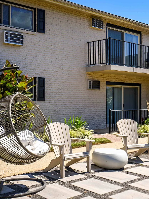 Charming apartment courtyard featuring stylish hanging chairs, lush greenery, and a sunlit patio area.