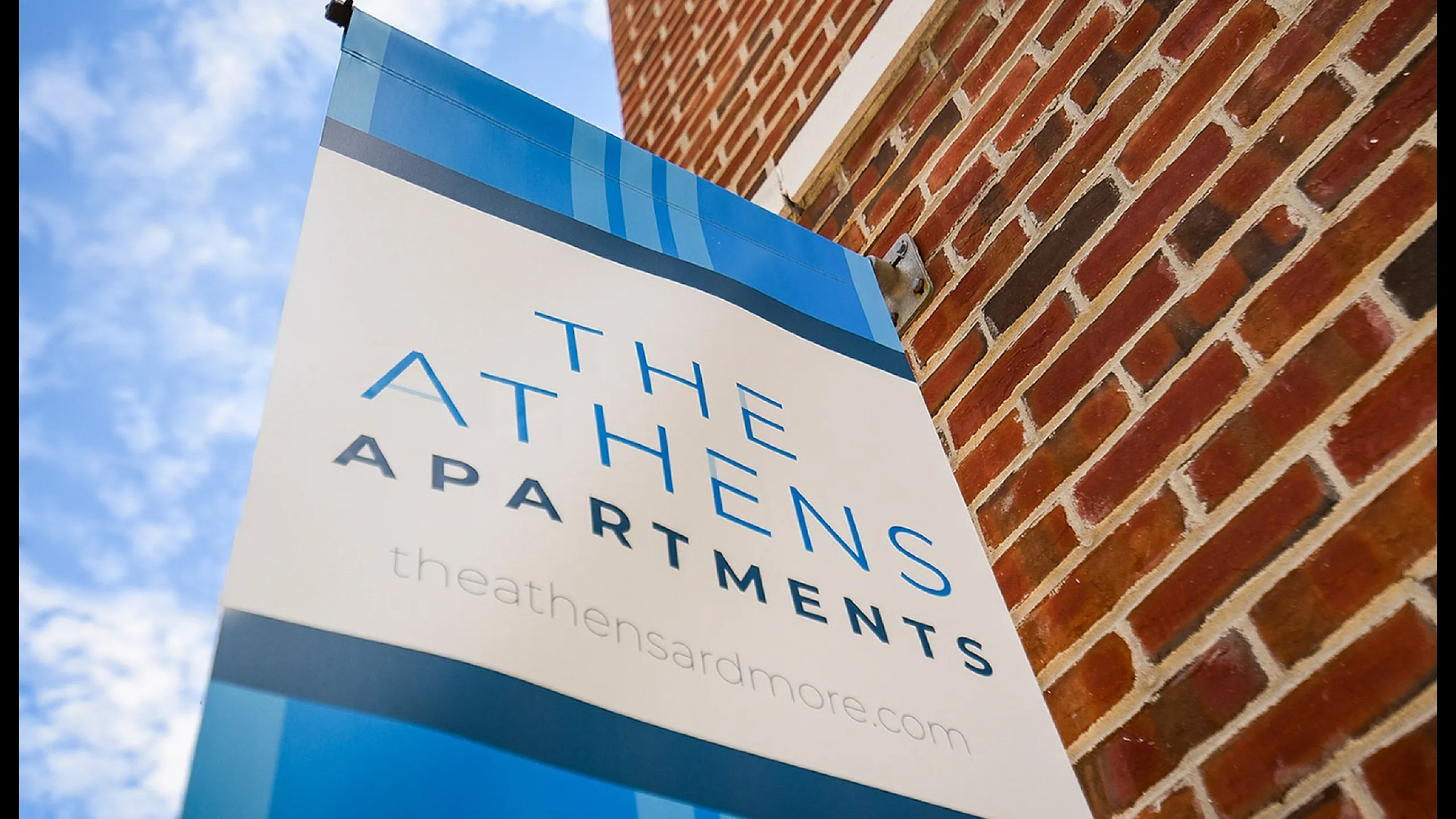Vibrant sign of The Athens Apartments against a clear blue sky, highlighting modern urban living.
