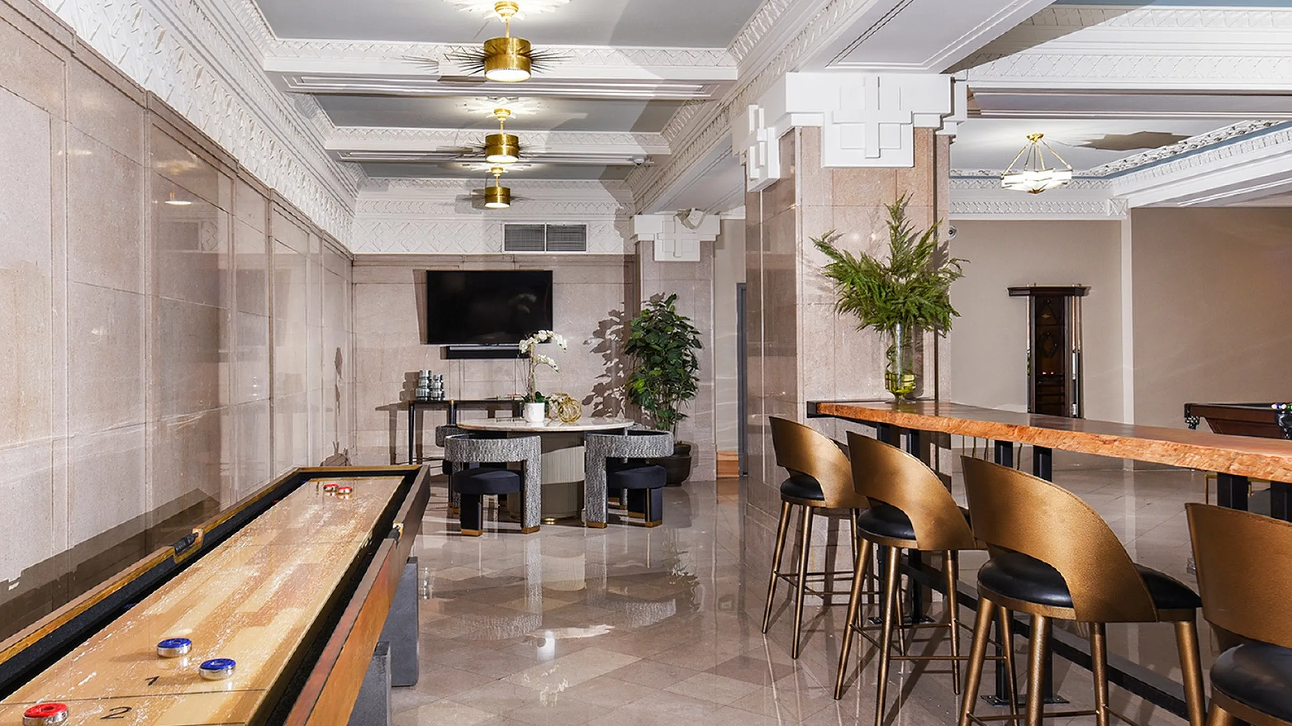 Elegant entertainment area with sleek shuffleboard table, modern bar seating, and stylish decor in a luxurious setting.