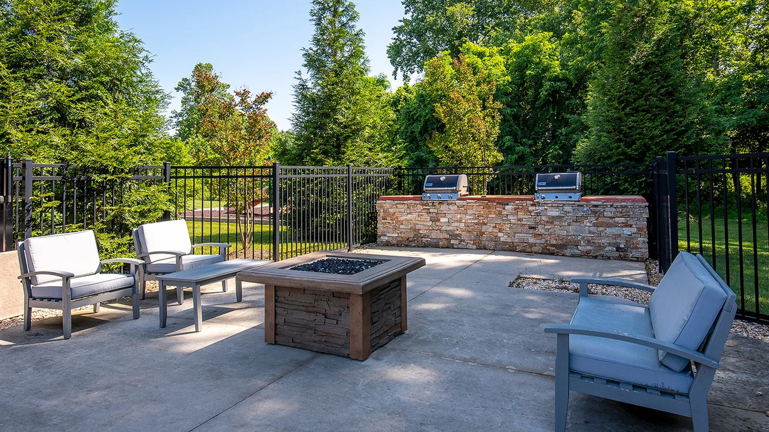 Charming outdoor patio with cozy seating, fire pit, and built-in grills, surrounded by lush greenery.