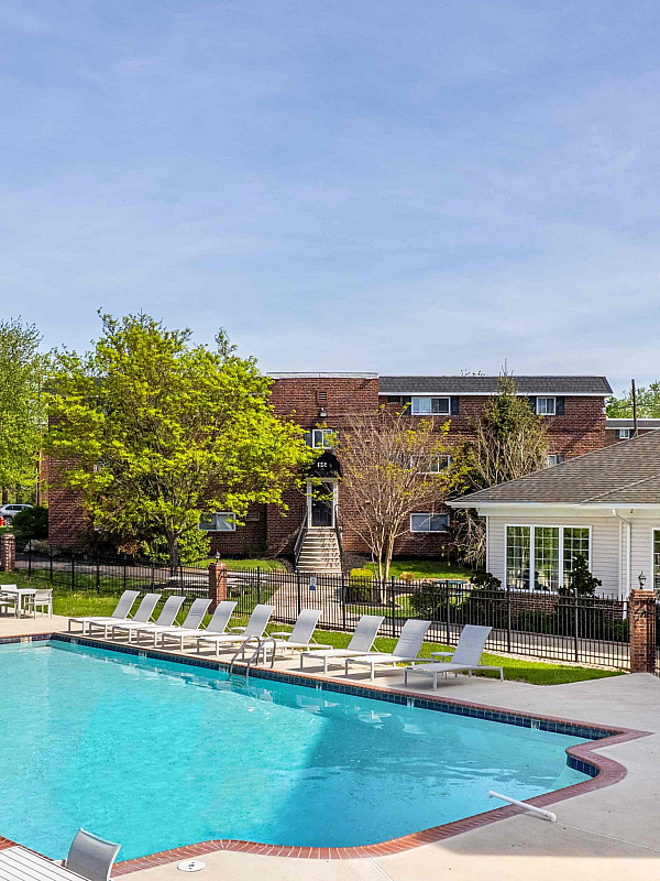Inviting apartment complex featuring a large outdoor pool surrounded by modern lounge chairs and lush greenery.