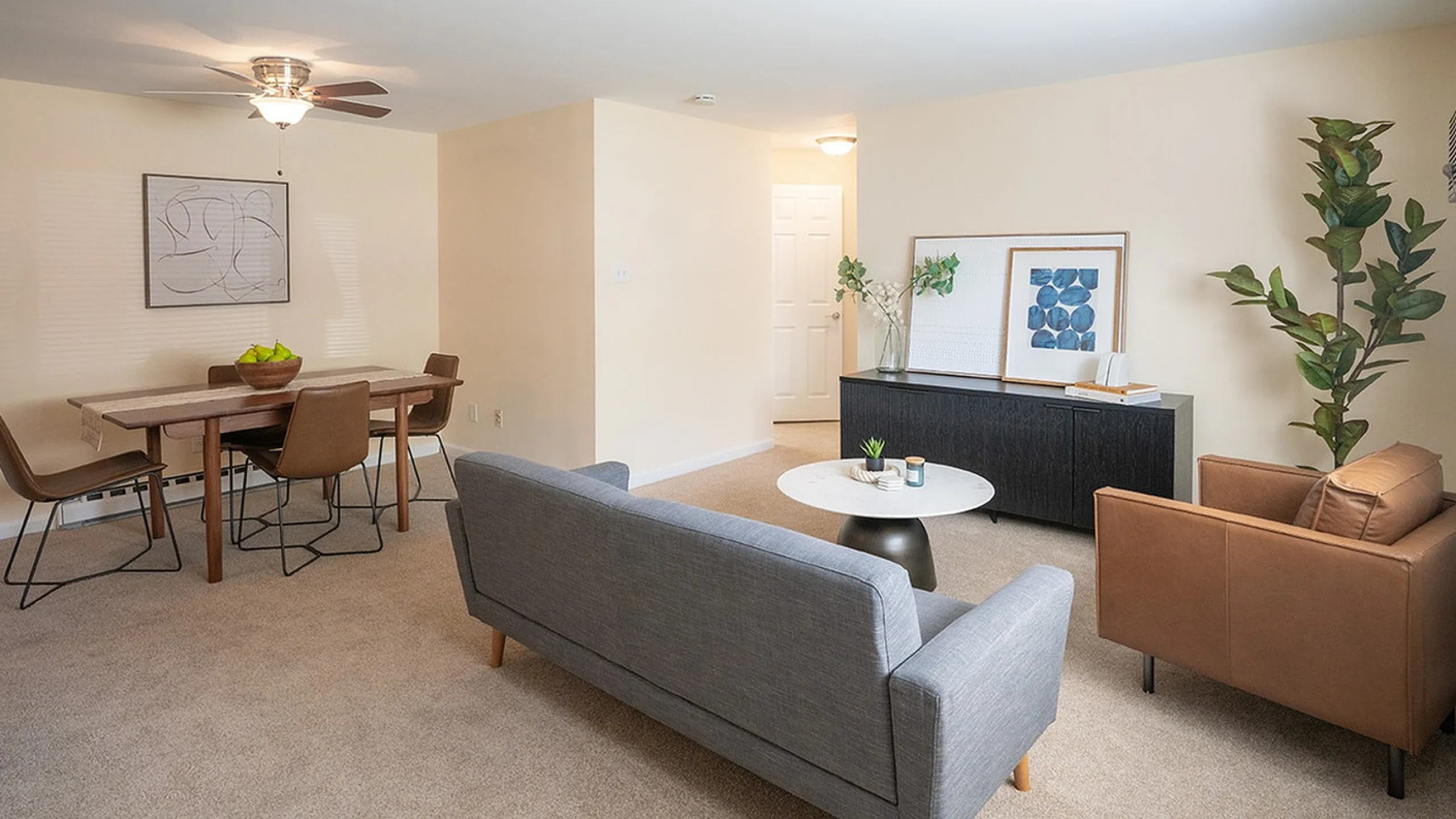 Inviting living and dining area with modern furniture, accentuated by a cozy gray sofa and elegant decor, offering a warm and stylish ambiance.