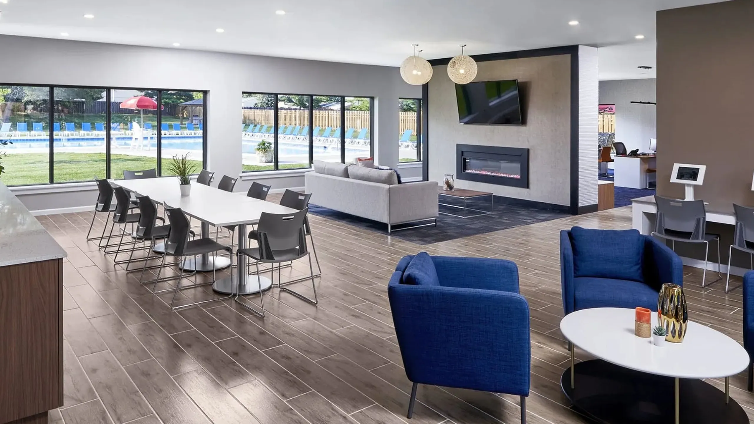 Luxurious community lounge featuring elegant seating areas, a modern fireplace, spacious dining table, and floor-to-ceiling windows overlooking a pristine pool area.