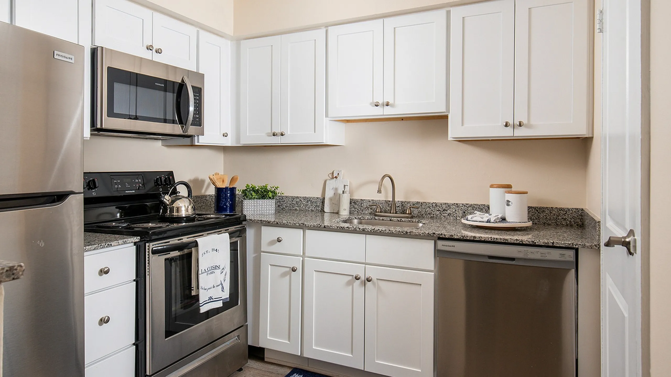 Modern apartment kitchen with sleek stainless steel appliances, pristine white cabinetry, and elegant granite countertops.