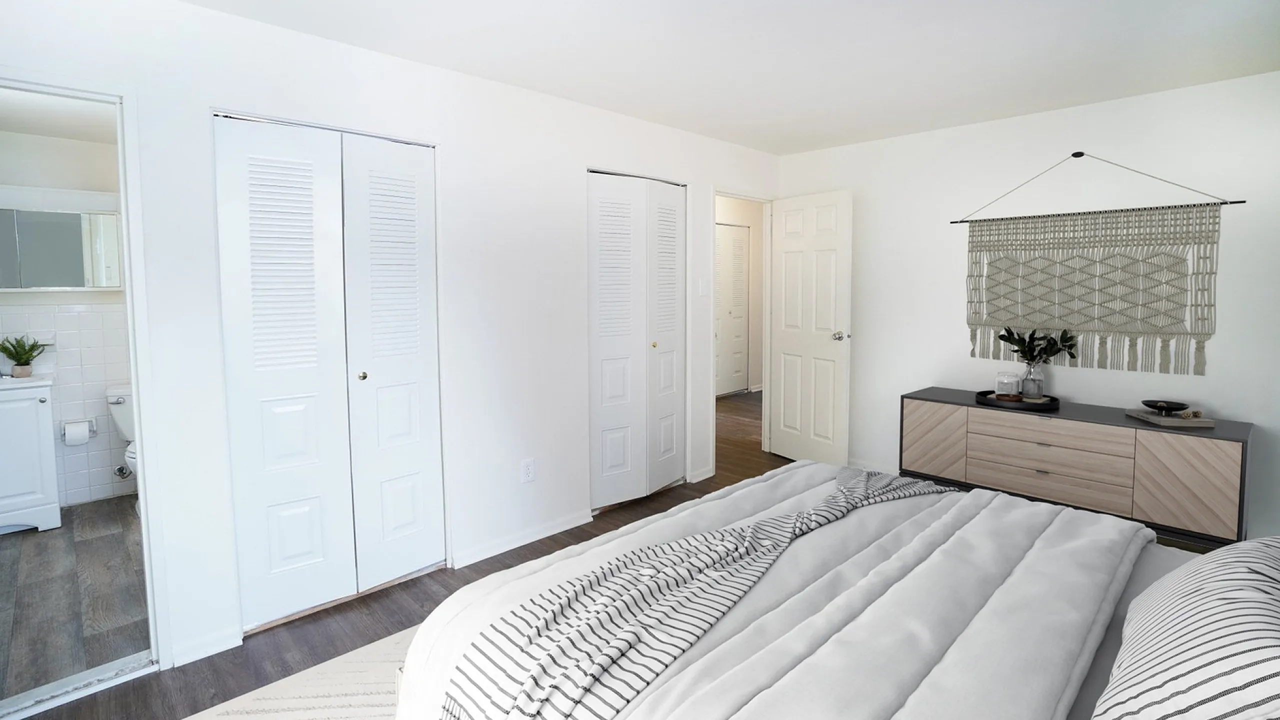 Bright and modern bedroom with cozy bedding, elegant wall hanging decor, and en-suite bathroom access.