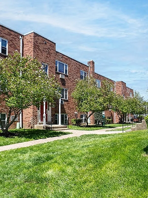 Charming brick apartment complex with lush green lawns and mature trees, offering a perfect blend of nature and comfort.