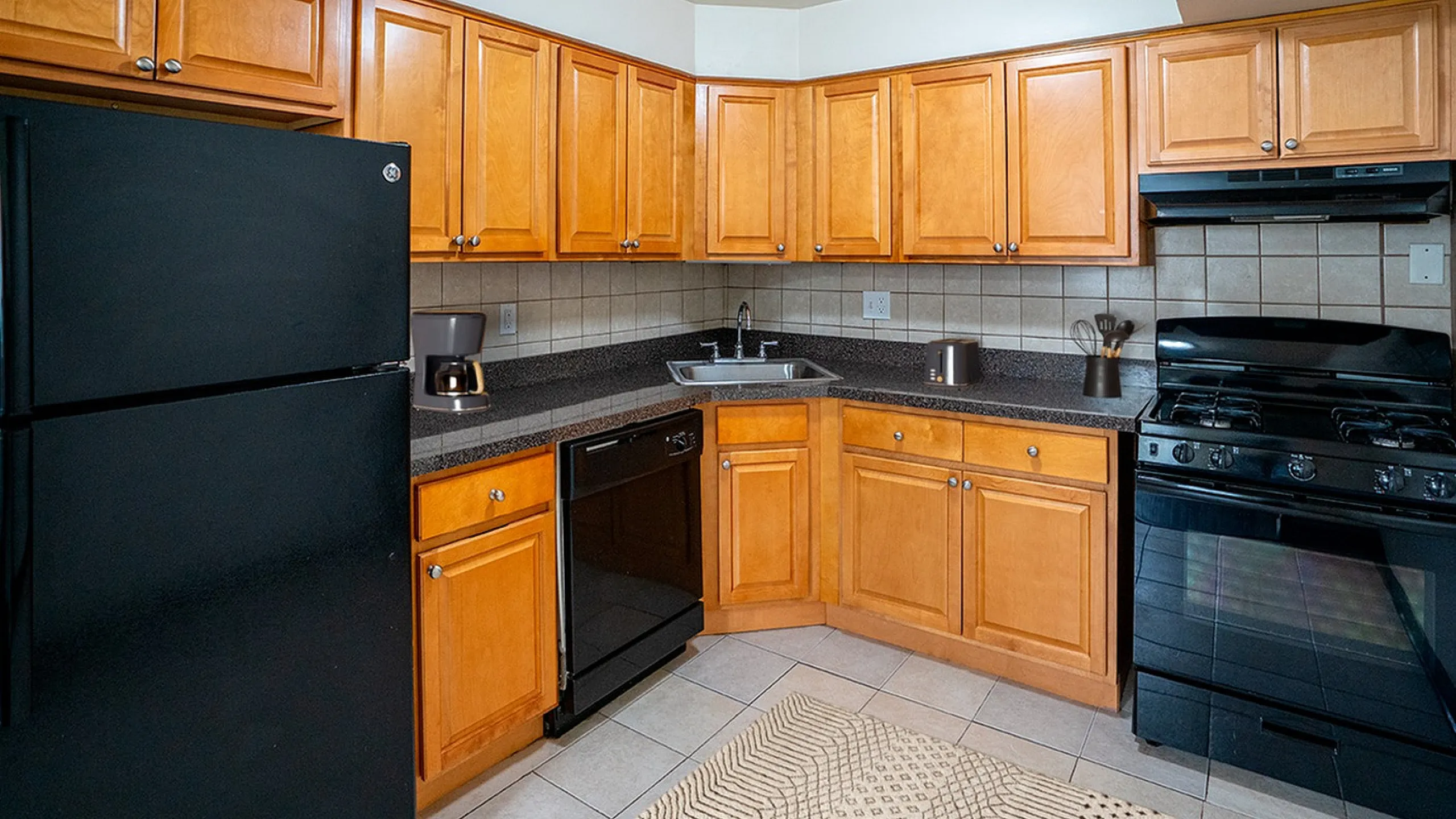 Inviting kitchen with warm wooden cabinets, sleek black appliances, and a modern countertop, perfect for culinary enthusiasts.