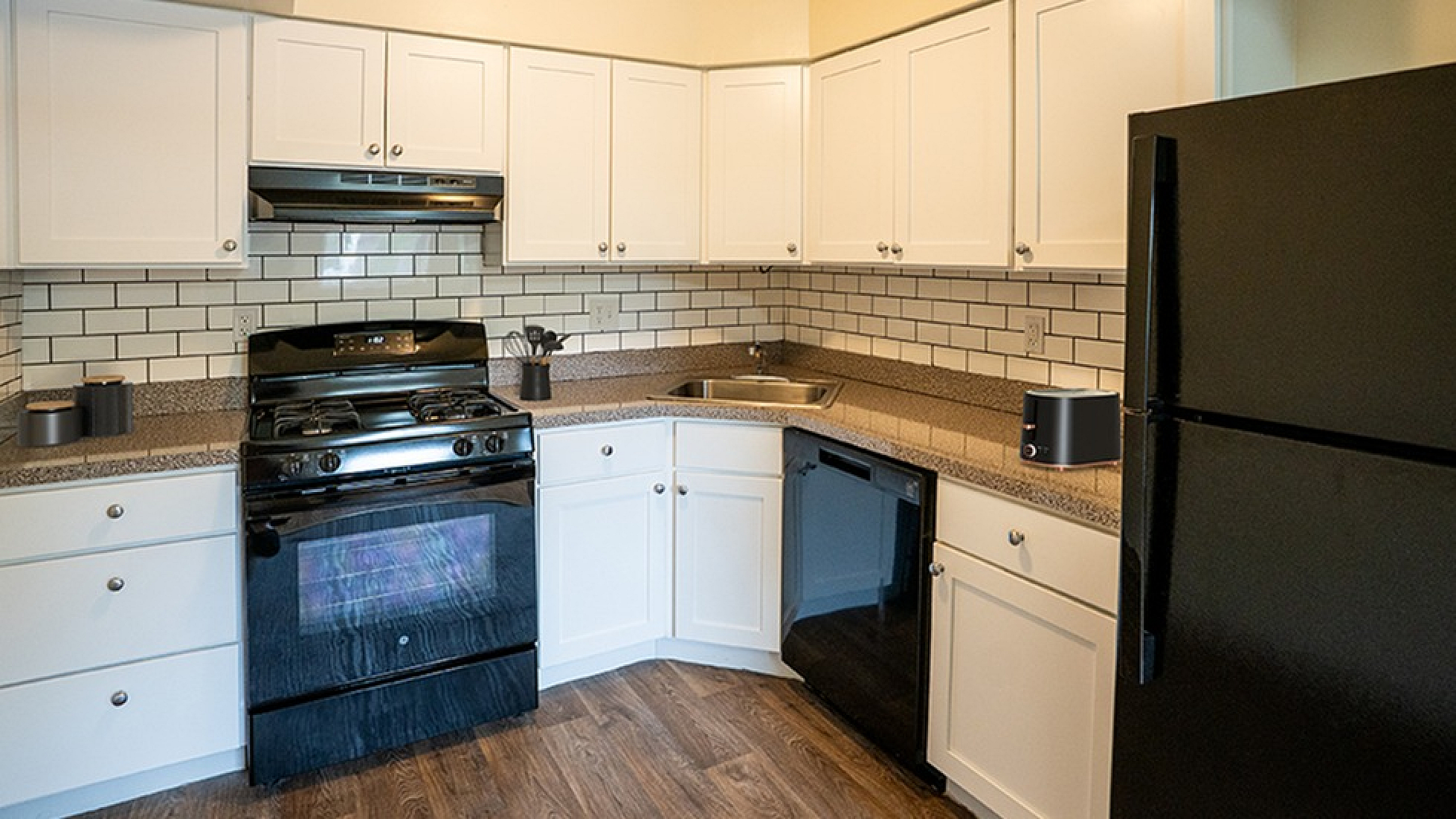 Modern kitchen with sleek black appliances, elegant white cabinetry, and stylish subway tile backsplash.