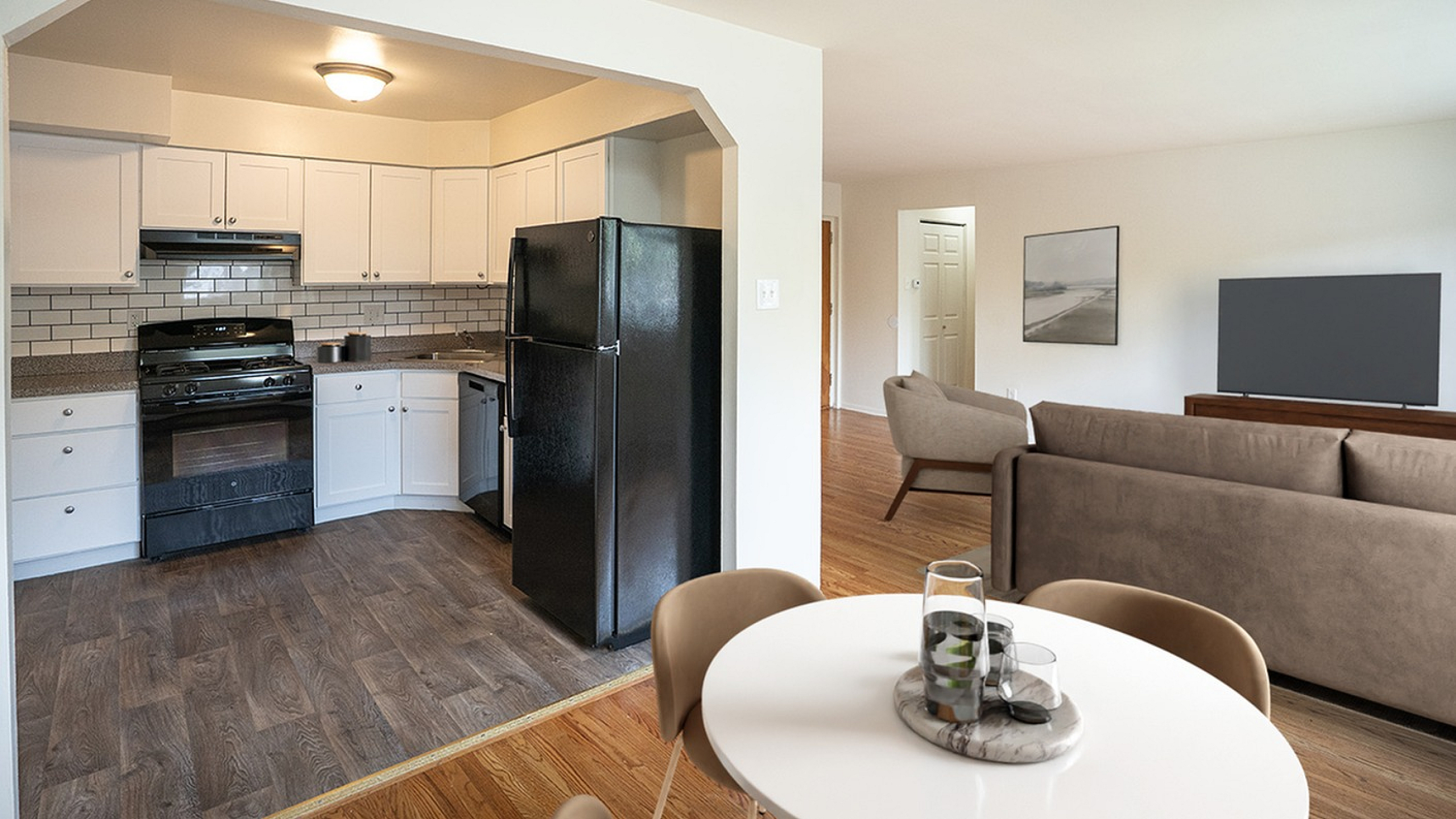 Inviting open-concept apartment showcasing a modern kitchen with white cabinets and a cozy living area with stylish decor.