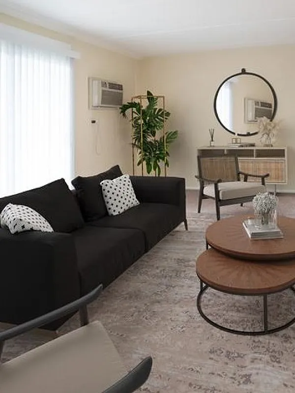 Bright and inviting living room with modern d&eacute;cor, featuring a sleek black sofa, stylish wooden coffee tables, and a wall-mounted TV.