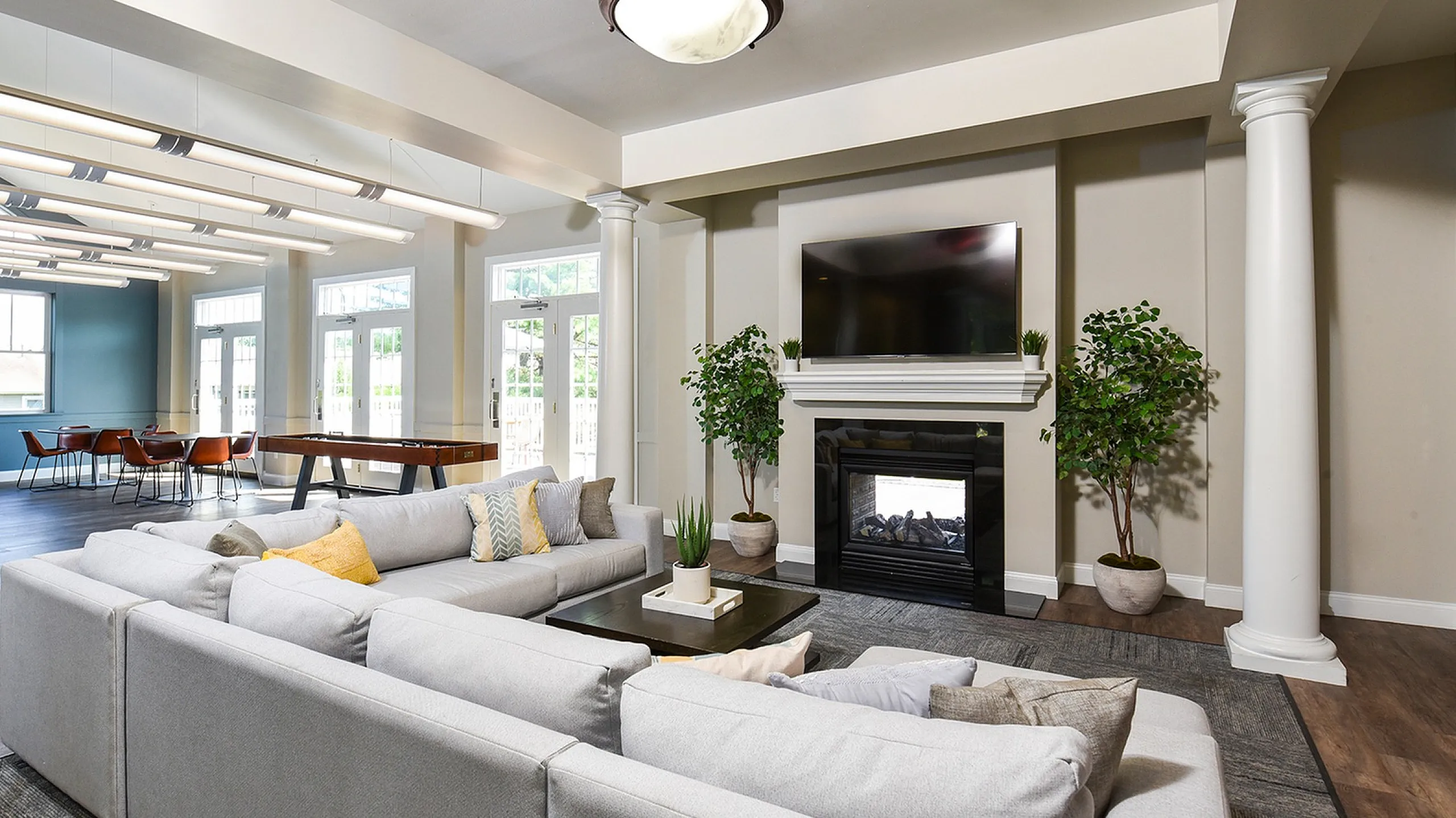 Luxurious modern living room with elegant decor, featuring a cozy sectional sofa, stylish fireplace, and wall-mounted TV. Natural light floods through expansive windows, highlighting the sophisticated design and dining area with sleek furni