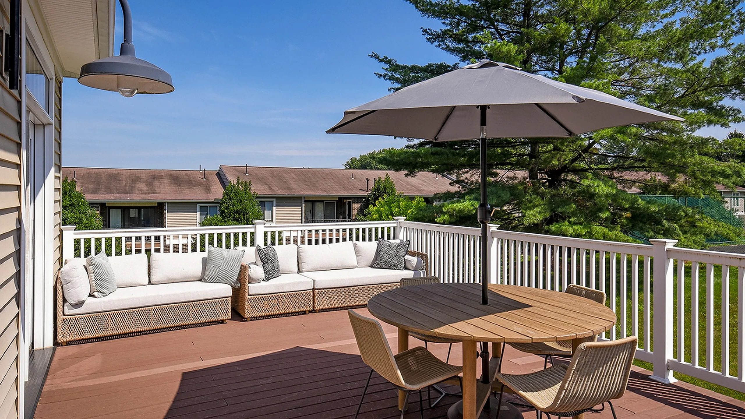 Charming outdoor deck featuring cozy wicker seating, a stylish umbrella-shaded table, and lush green surroundings.