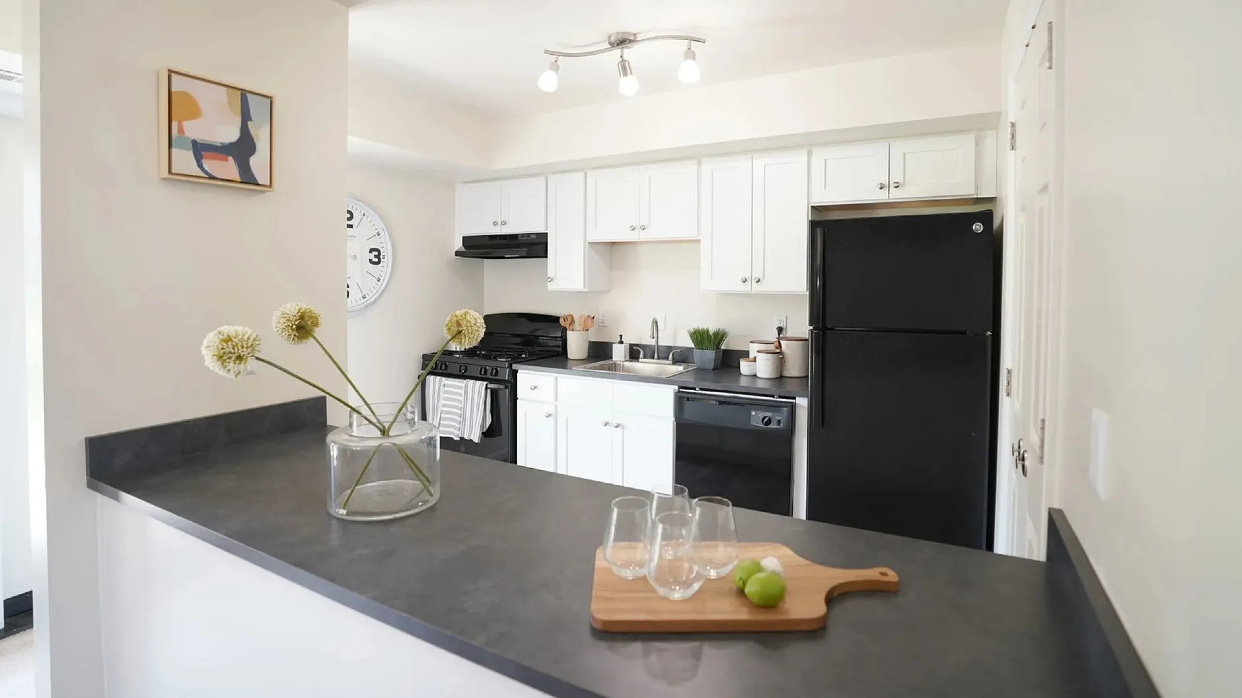 Modern kitchen with elegant black appliances, stylish white cabinetry, and chic decor, featuring a cozy breakfast bar.