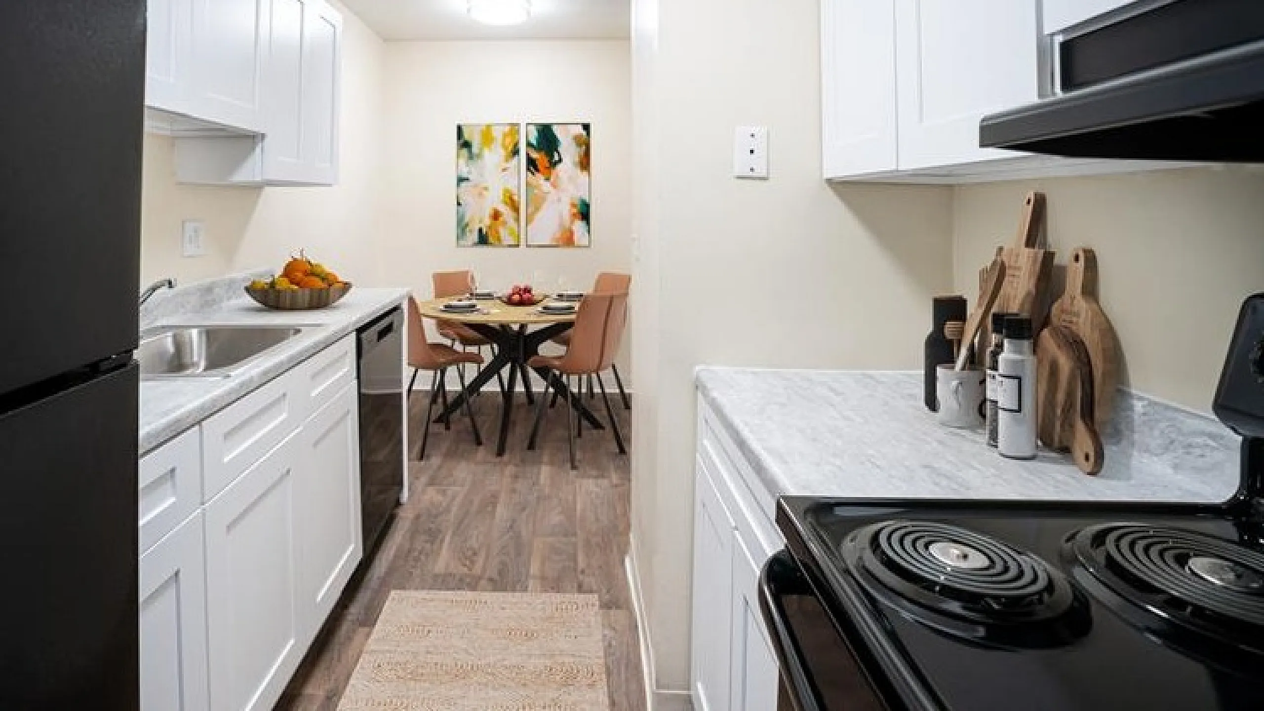 Chic galley kitchen with modern white cabinetry, sleek countertops, and stainless steel appliances leading to an elegant dining area with contemporary art.