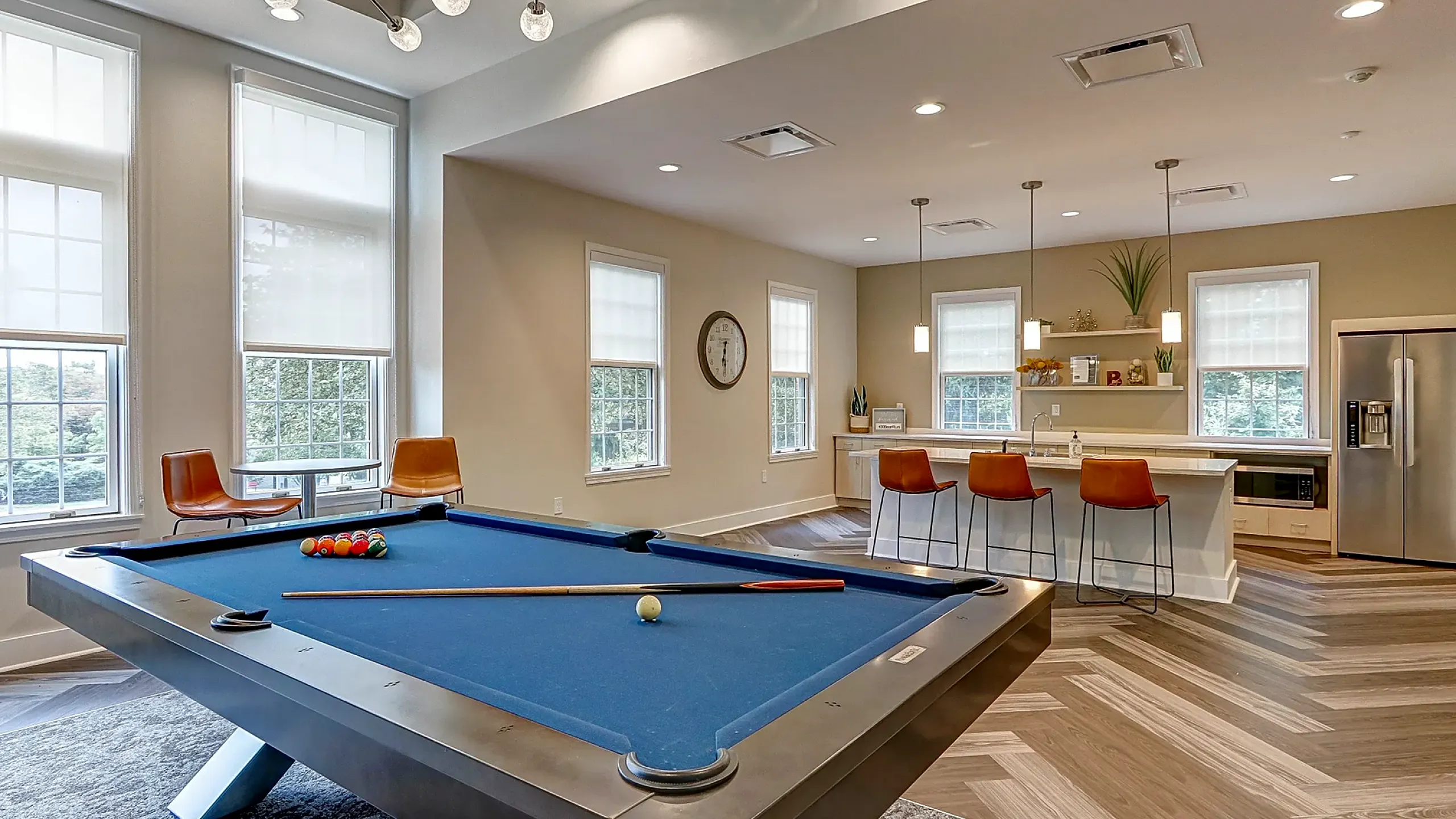 Luxurious recreation room featuring a sleek billiard table and modern kitchen with stylish bar seating and natural light.
