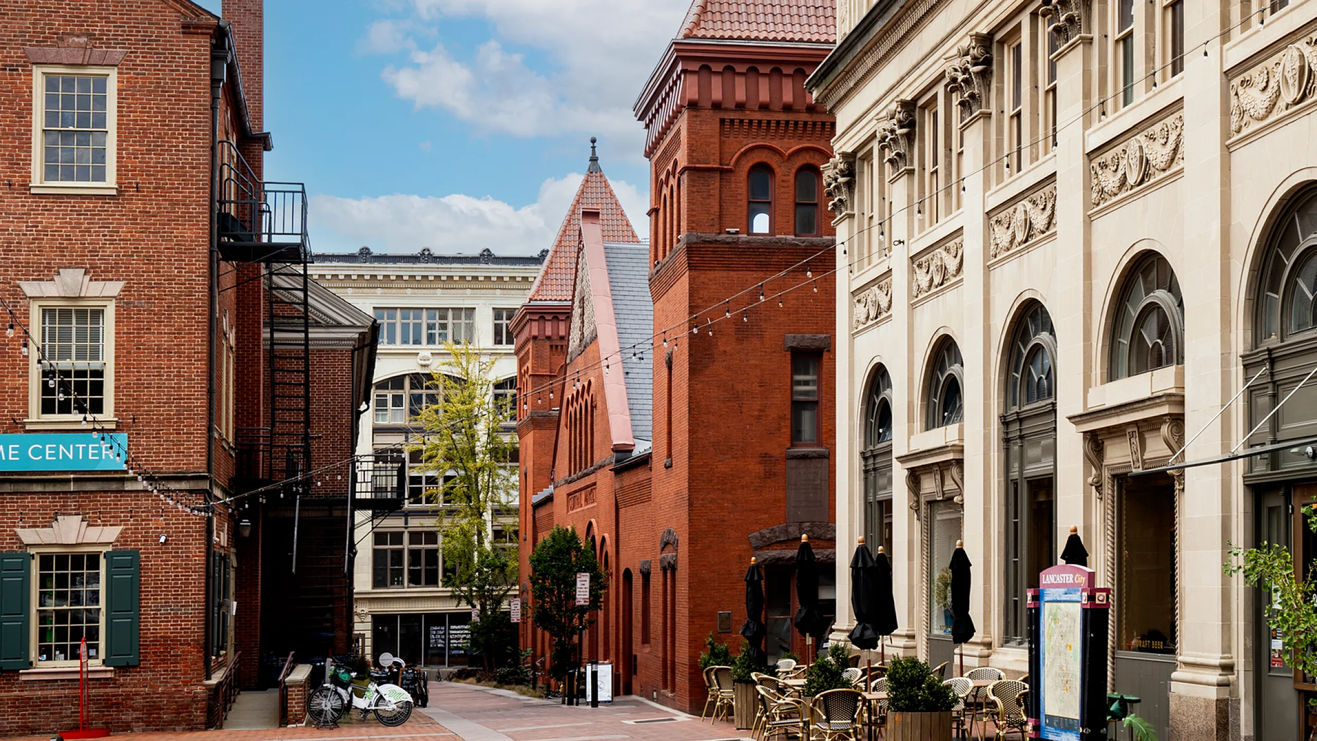 Charming urban scene featuring historic red brick buildings with architectural details, inviting outdoor seating, and a bright blue sky.