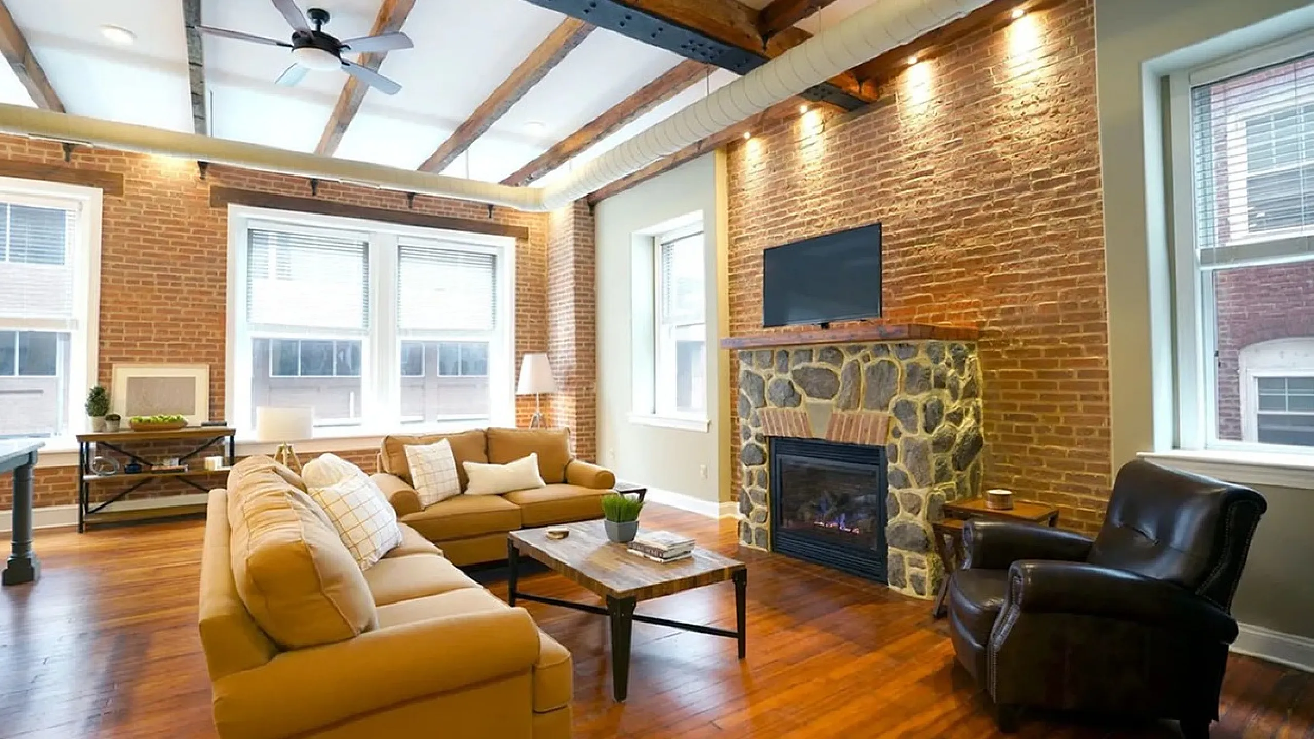Chic and inviting living room featuring exposed brick walls, wooden beams, and a cozy stone fireplace, perfect for relaxing or entertaining.