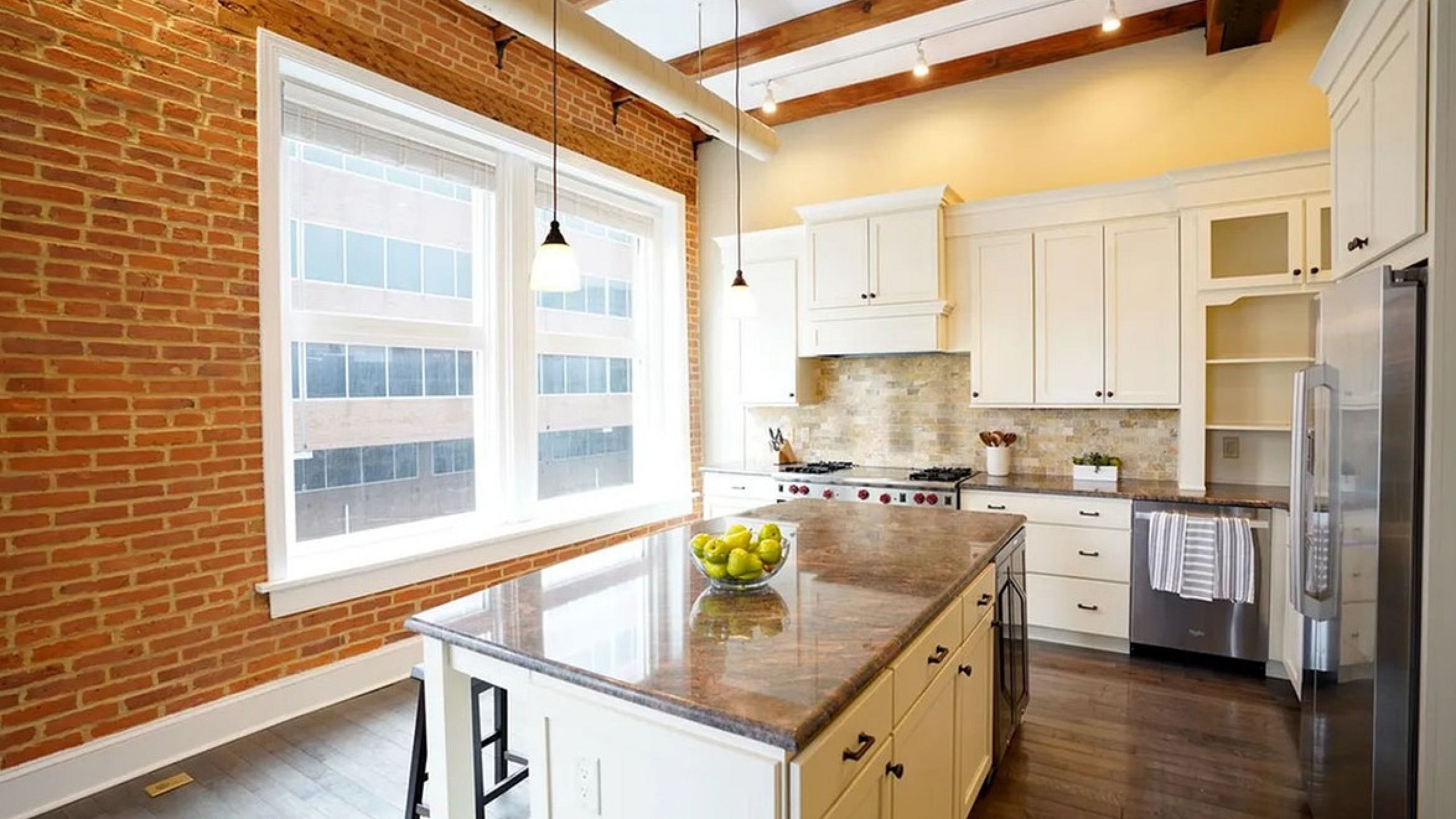 Charming modern kitchen with rustic brick walls, elegant white cabinetry, and a spacious island, perfect for culinary enthusiasts.