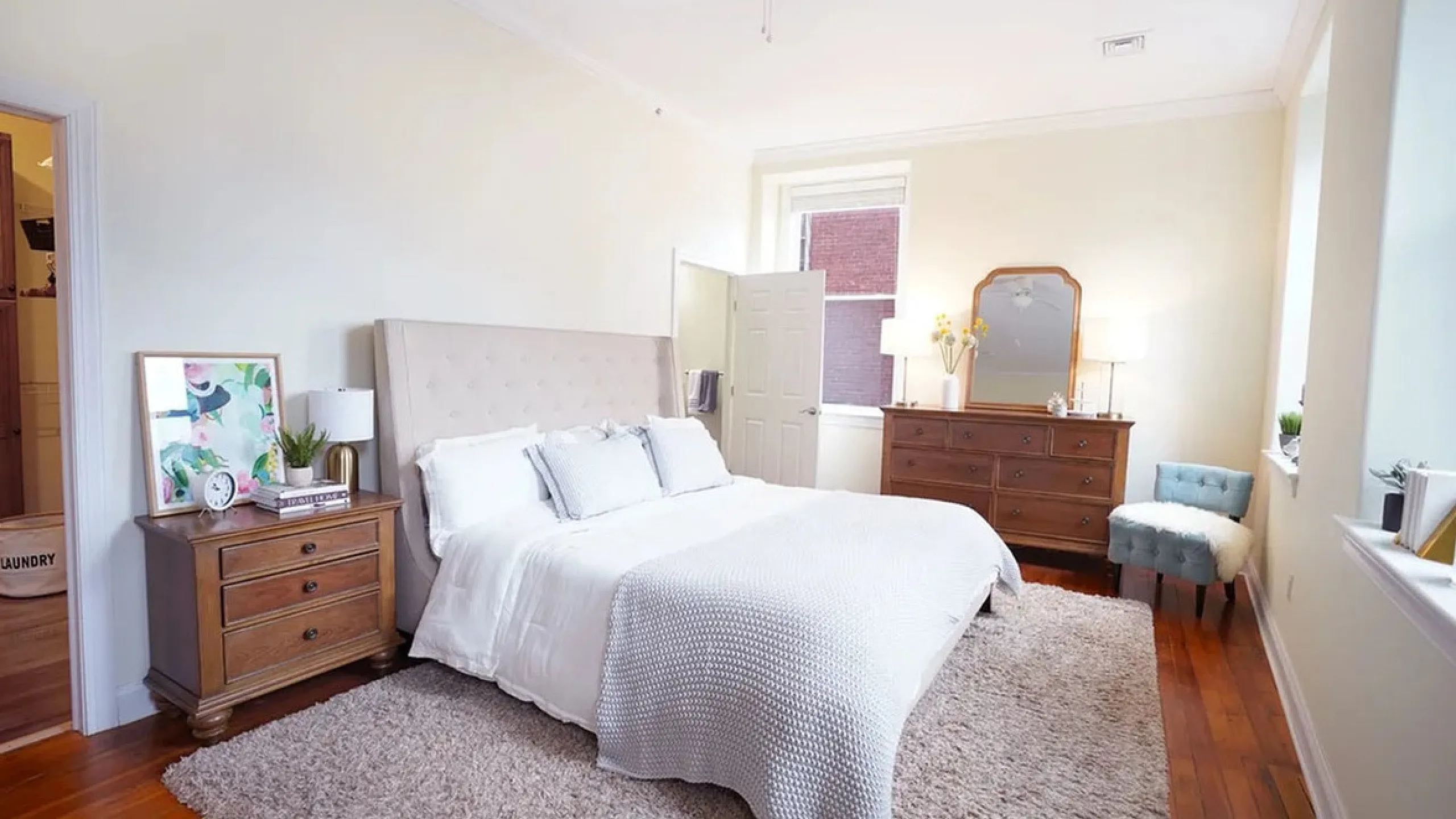 Bright and inviting bedroom with elegant hardwood flooring, plush area rug, and cozy bedding, enhanced by natural light pouring through large windows.