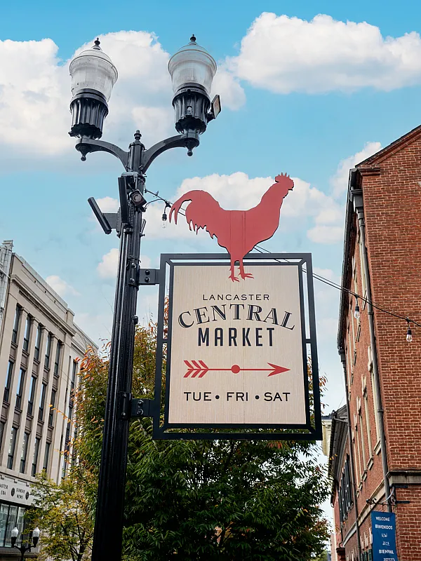 Charming street view featuring the Lancaster Central Market sign with a red rooster silhouette, set against a vibrant urban backdrop and a clear blue sky.