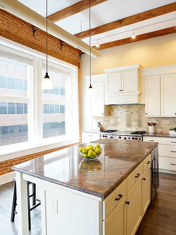 Elegant kitchen with exposed brick wall, modern stainless steel appliances, and large island countertop, bathed in natural light from tall windows.