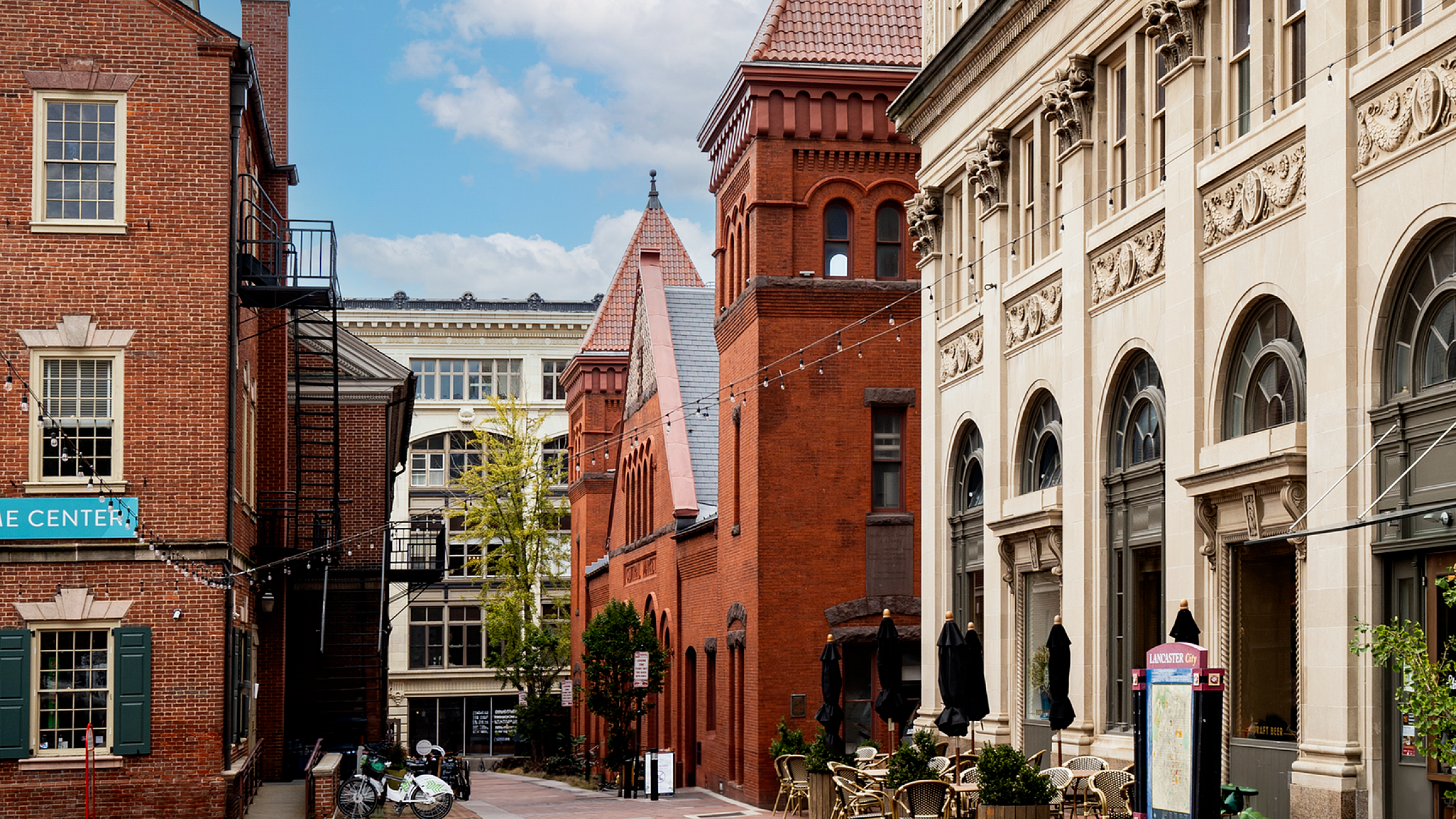 Charming urban street with historic architecture, elegant facades, and inviting outdoor cafe seating under a bright blue sky.