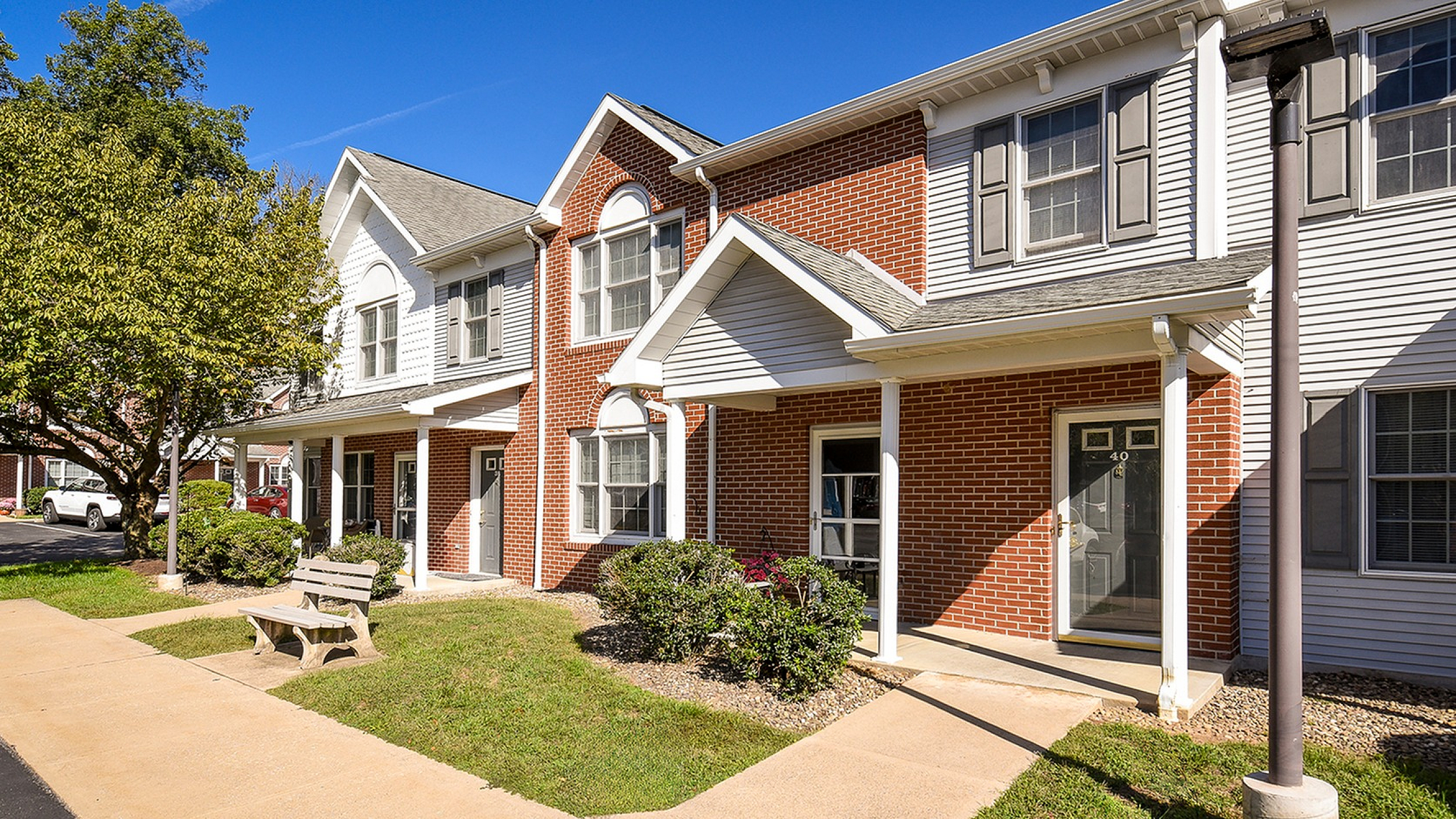 Charming townhouse with brick exterior, inviting front porch, and lush landscaping under a bright blue sky.