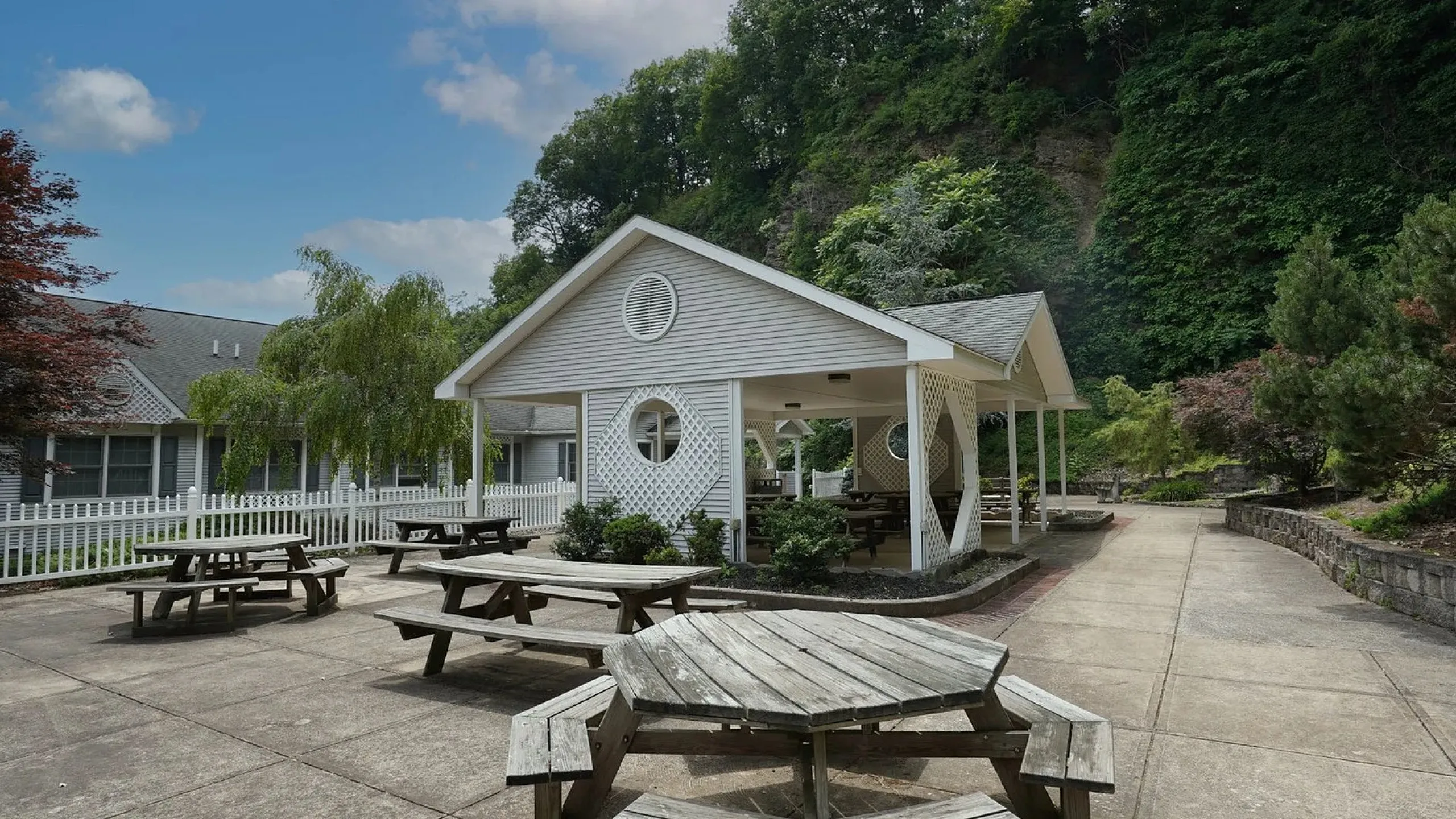 Charming outdoor communal area with wooden picnic tables and a stylish pavilion, surrounded by lush greenery for a peaceful retreat.