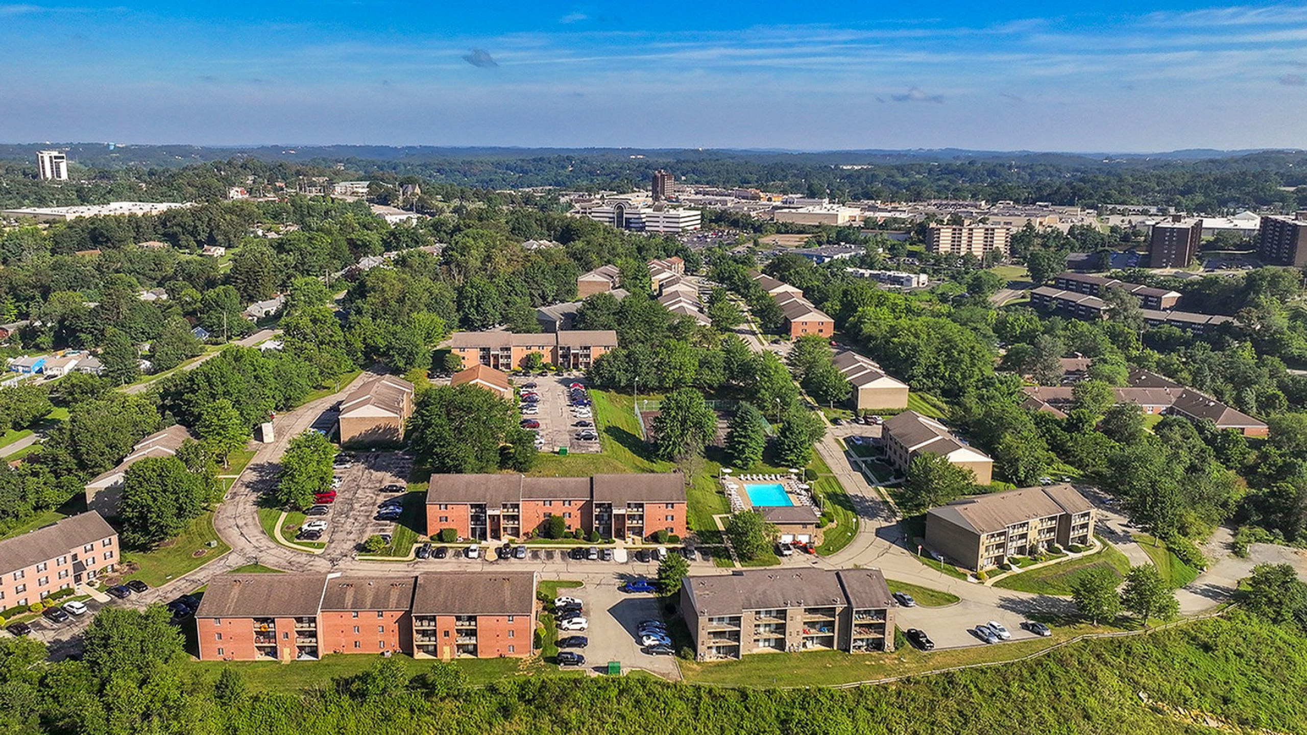 Charming aerial view of a vibrant apartment community surrounded by lush greenery and a sparkling pool, perfect for tranquil living.