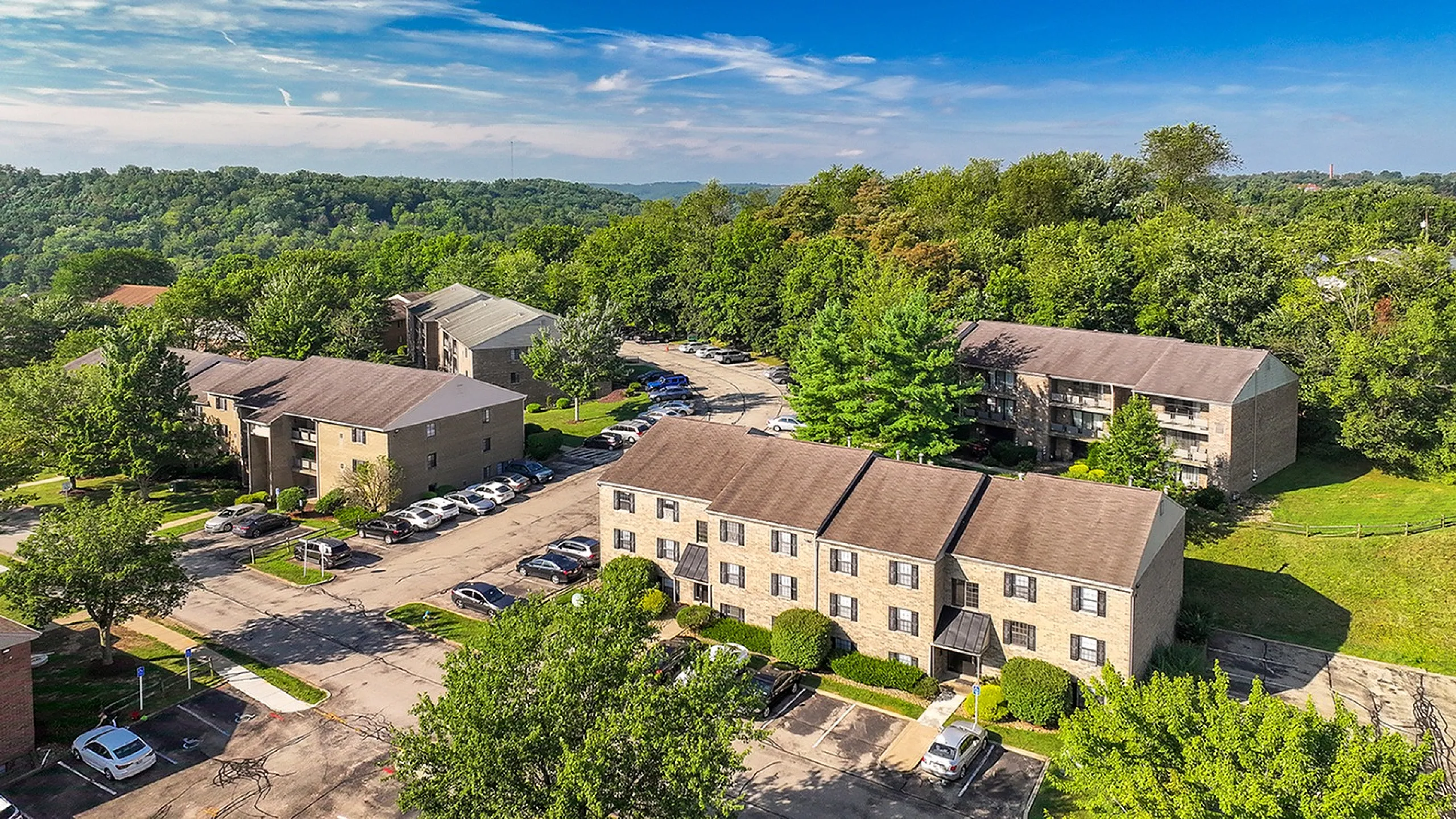 Charming apartment complex surrounded by lush greenery, featuring ample parking and scenic views under a vibrant blue sky.