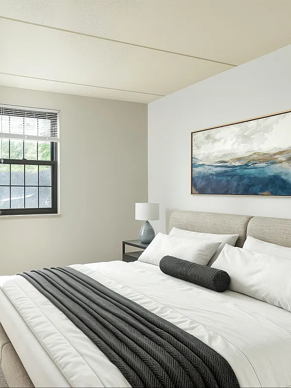 Bright and inviting bedroom with modern decor, featuring a cozy bed, elegant artwork, and abundant natural light through a large window.