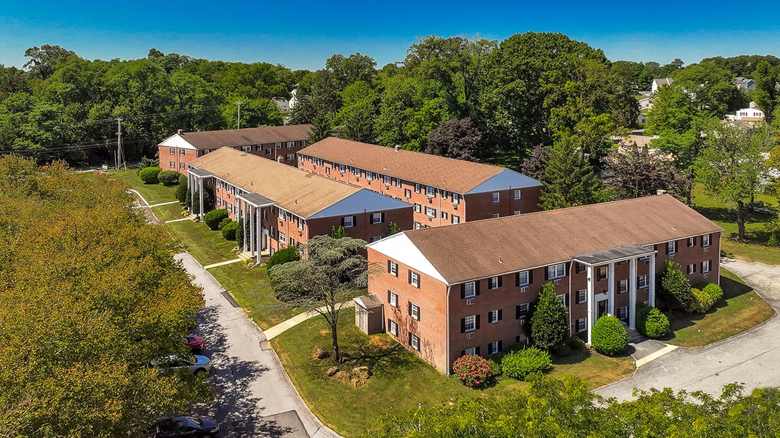 Charming brick apartment complex surrounded by lush greenery, featuring classic architectural design and ample parking space.
